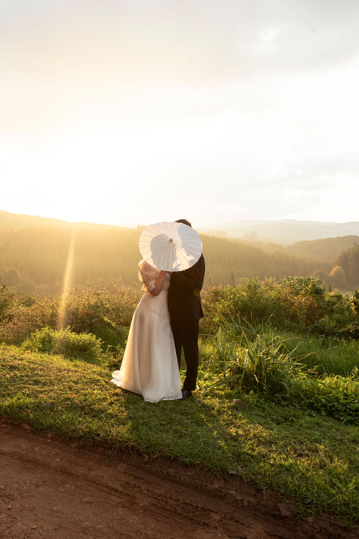 Bride in a wide-brimmed hat walking through a field at sunset