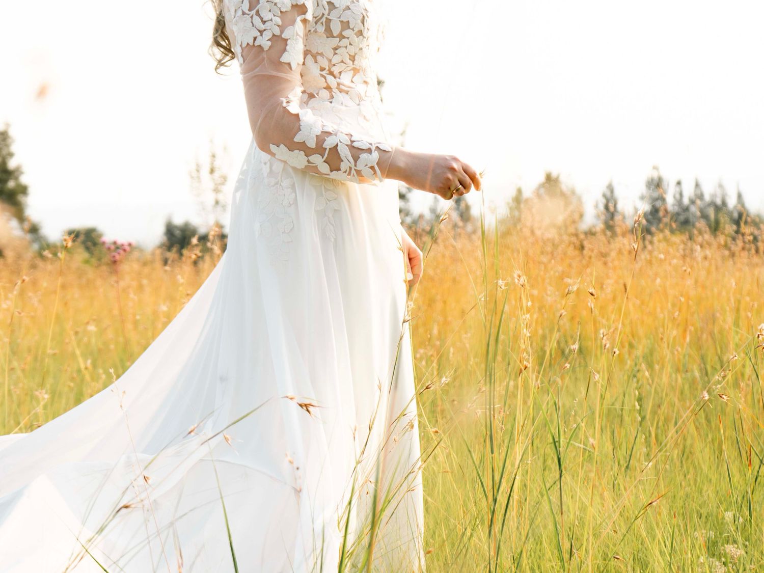 Bride in a lace wedding dress walking through a grassy field