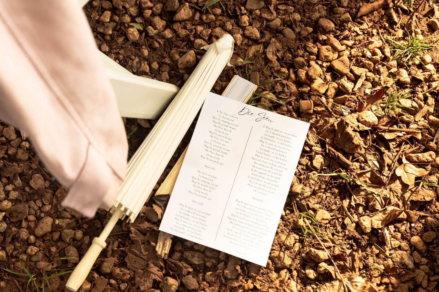 Hand holding a handwritten wedding stationery card above autumn leaves