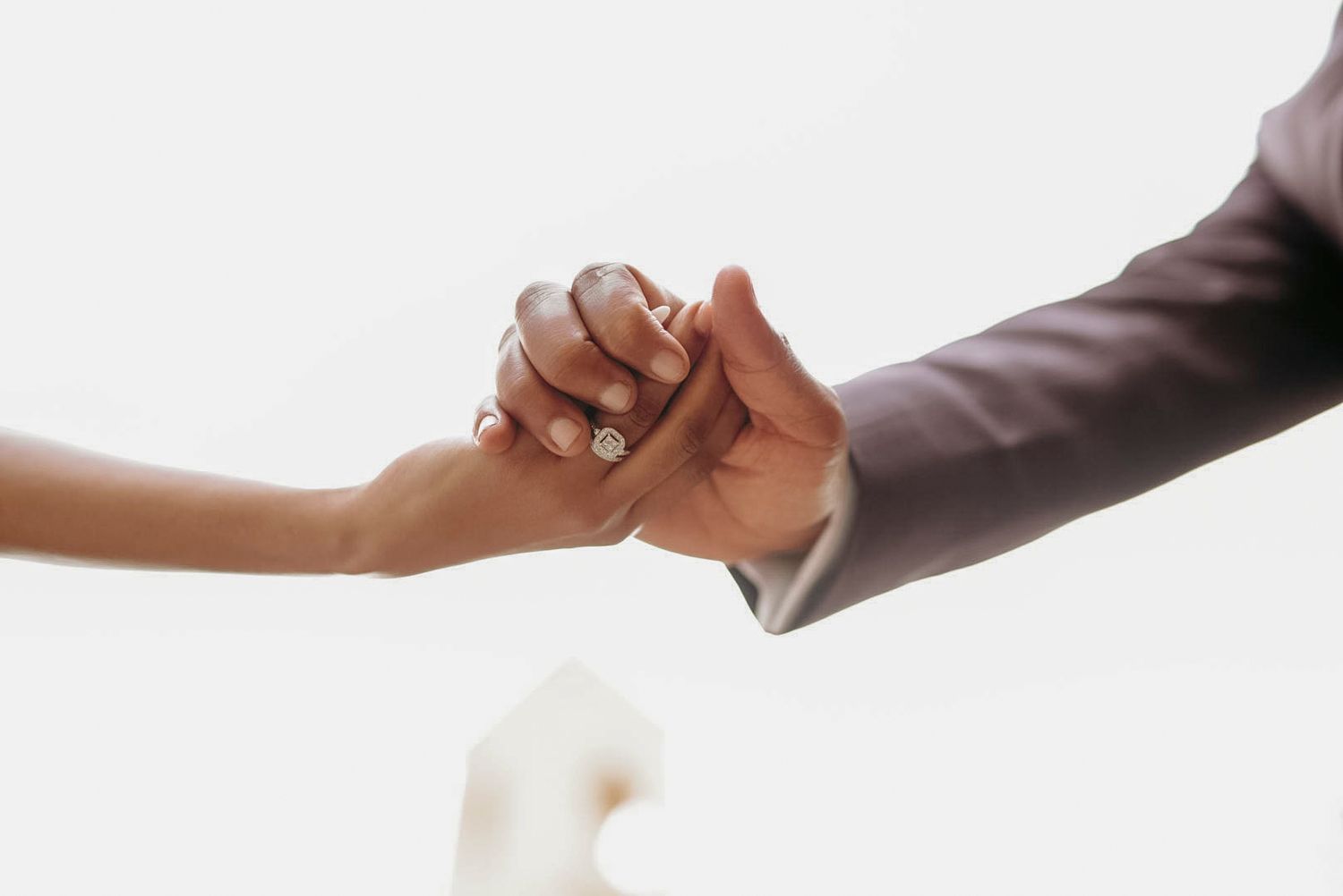Close-up of the bride and groom holding hands with a small white flower