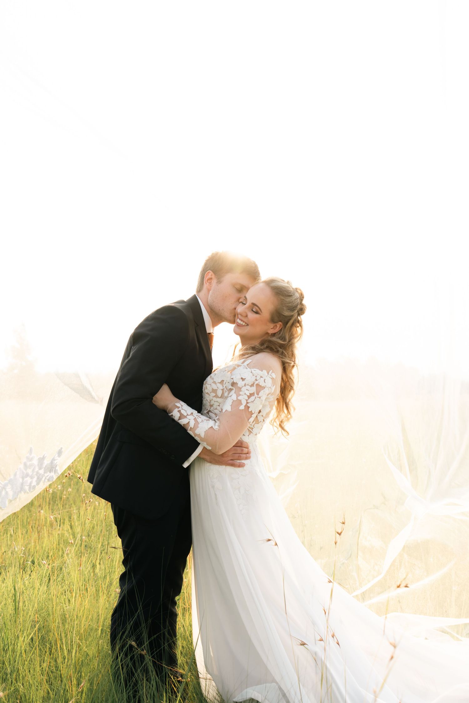 Groom kissing the bride in a golden field at their wedding