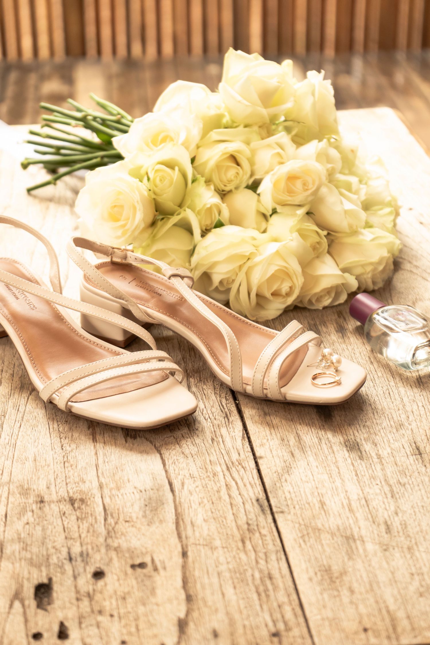 Bridal bouquet of white roses next to wedding shoes on a wooden floor