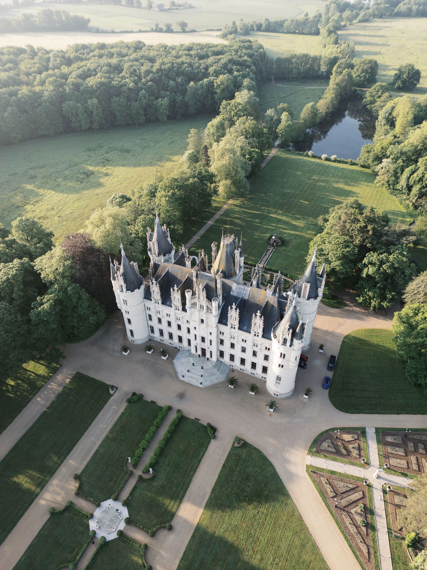 Aerial views of a grand white Gothic Revival Chateau Challain castle with ornate spires and manicured gardens in a lush countryside setting.