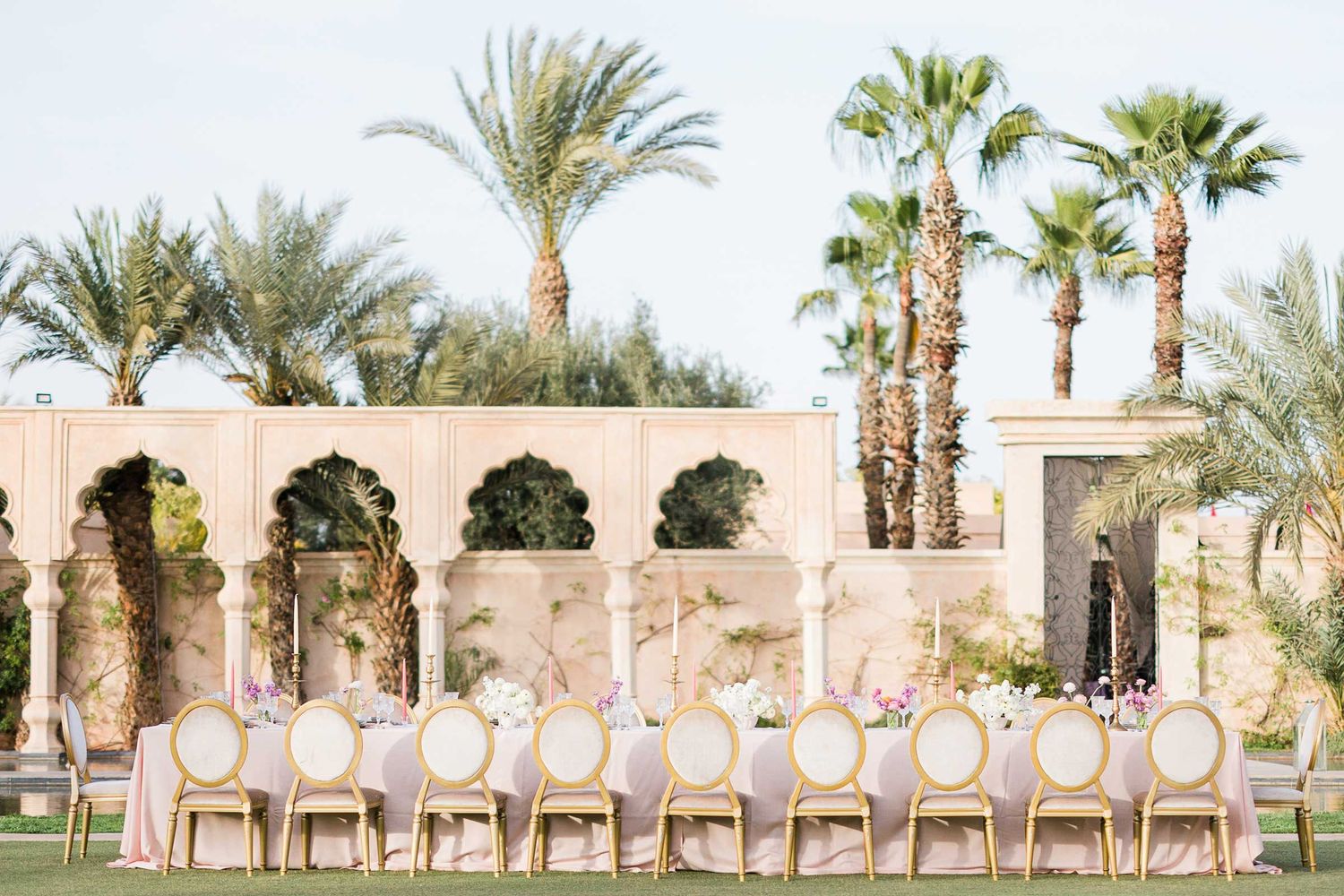 Palm trees line a desert resort pool deck with white lounge chairs arranged in a row against a clear blue sky.