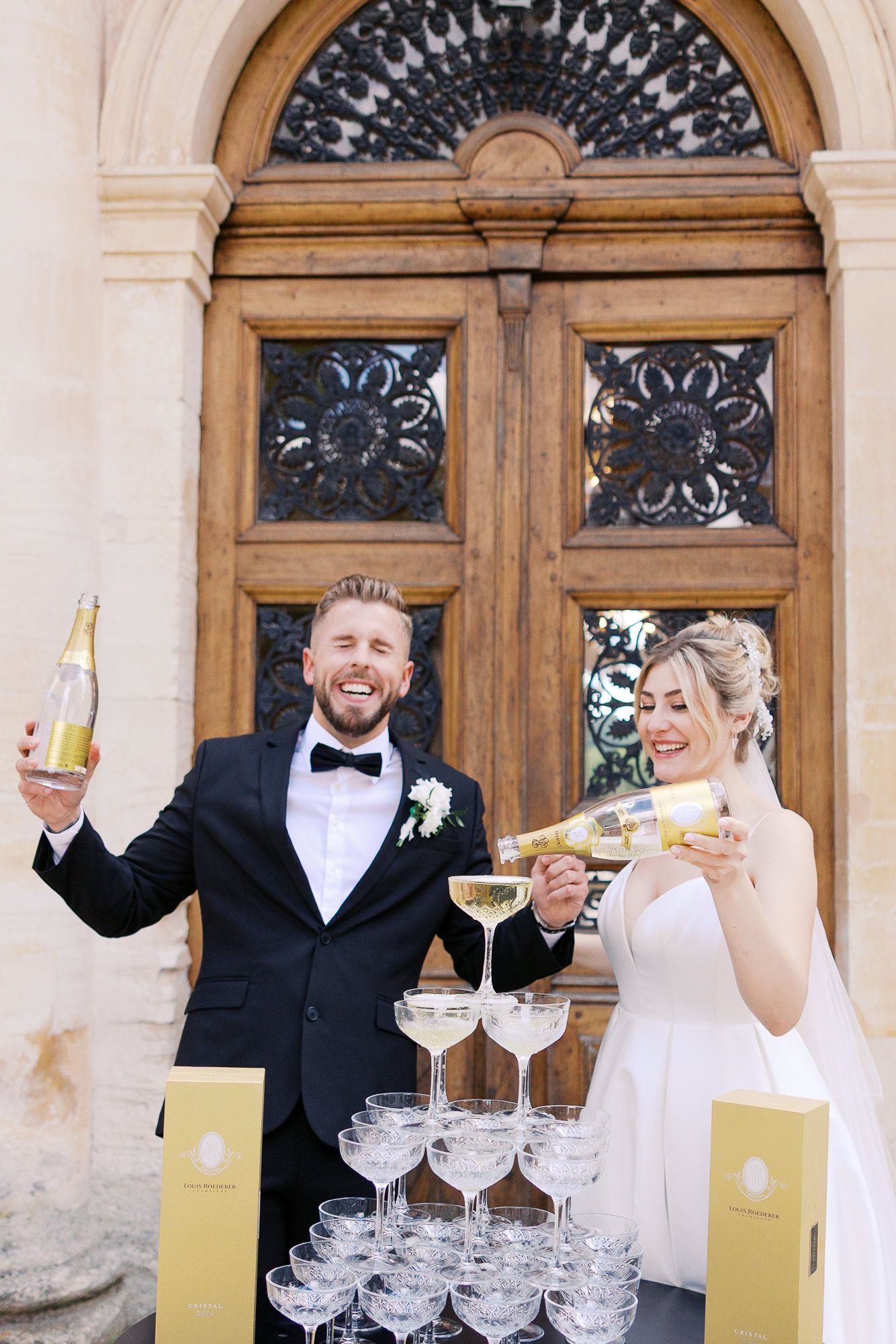 A group celebrates with champagne tower pouring at an elegant venue with ornate wooden doors and arched architecture at Château Martinay.