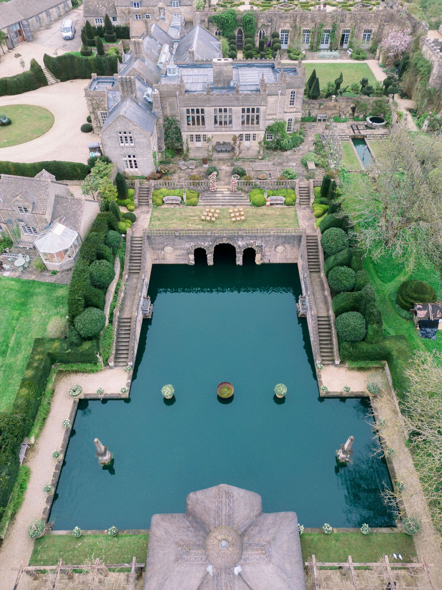 Aerial view of a historic mansion's rectangular reflecting pool with stone steps and manicured gardens in England.