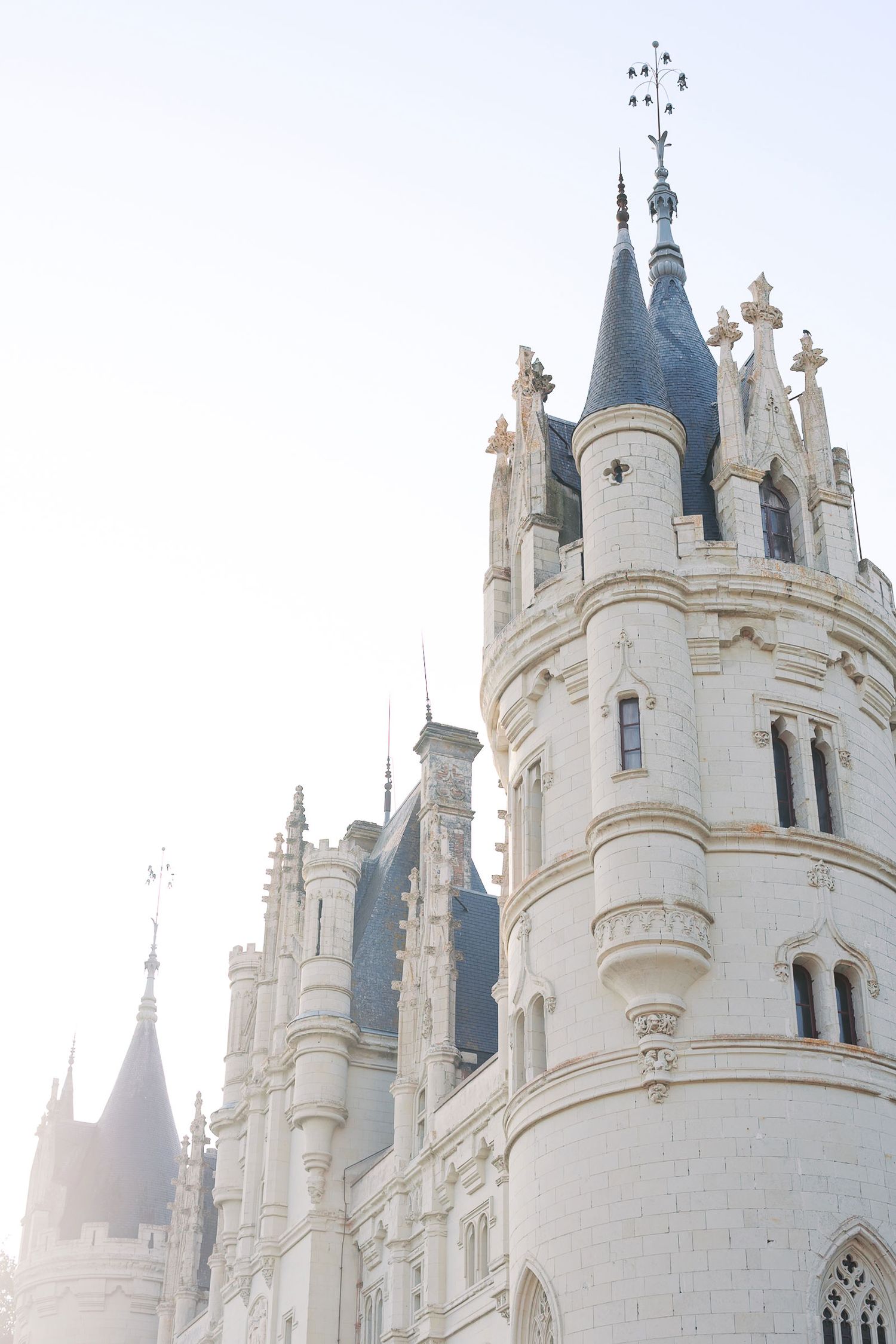 White castle spires with ornate Gothic architecture rise against a bright sky at Chateau de Challain in France.