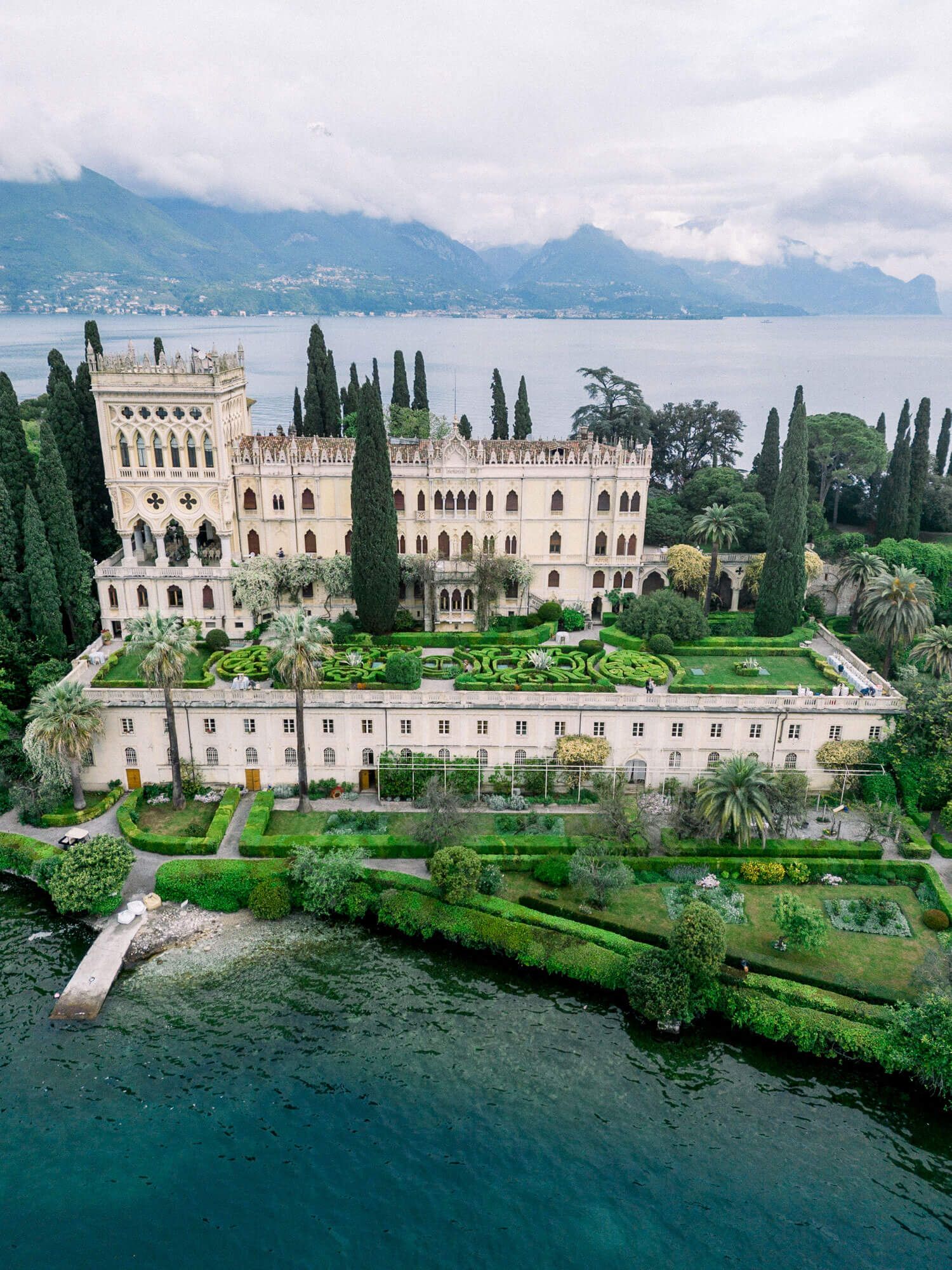 Stunning aerial views of the historic Isola del Garda villa and its manicured gardens along Lake Garda's shoreline in Italy.