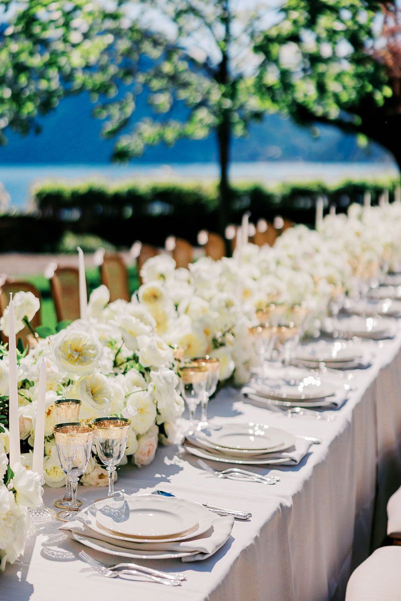 Elegant white wedding reception table setting with floral centerpieces and crystal glassware.