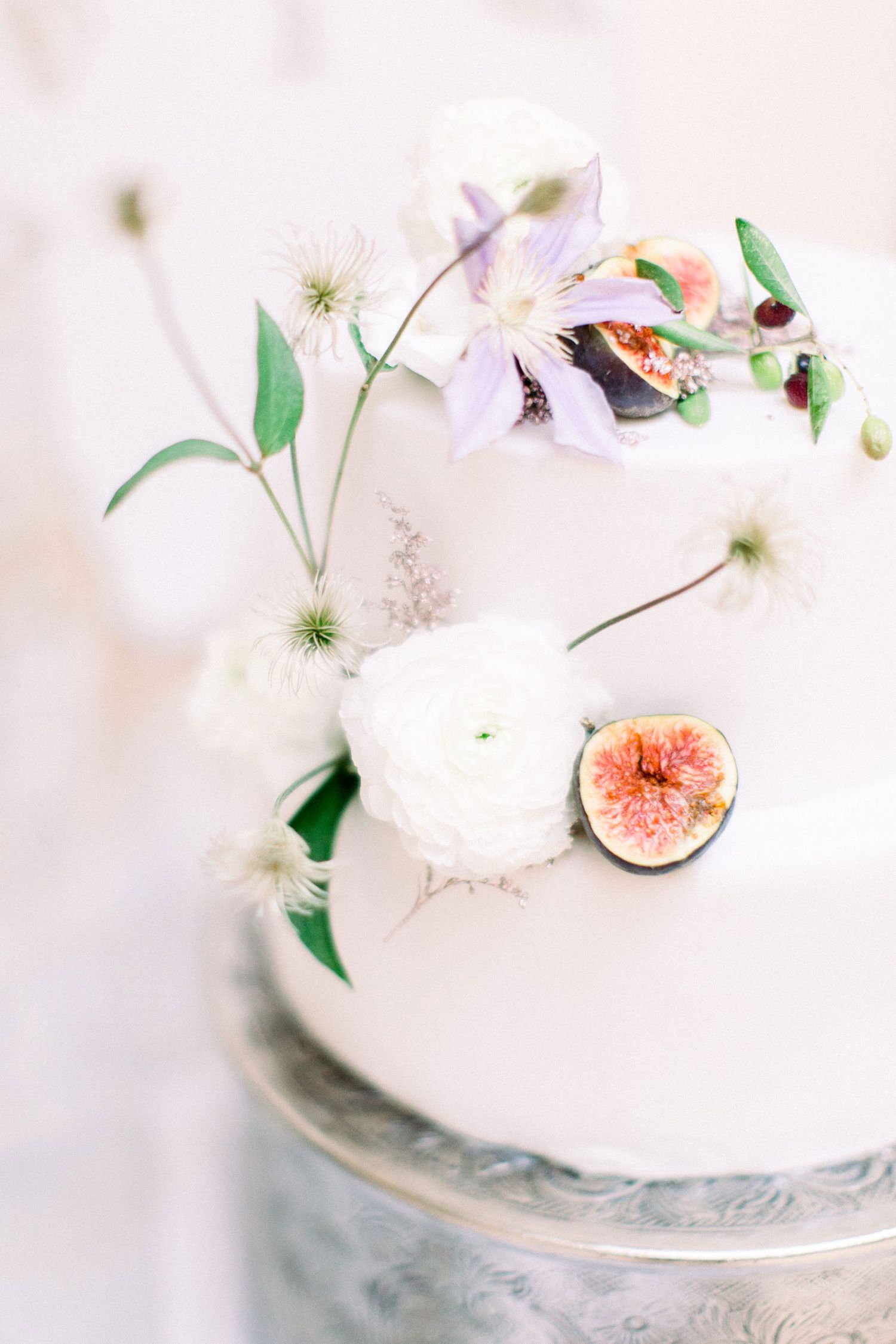 Elegant white wedding cake decorated with fresh figs and delicate white flowers on a light background.
