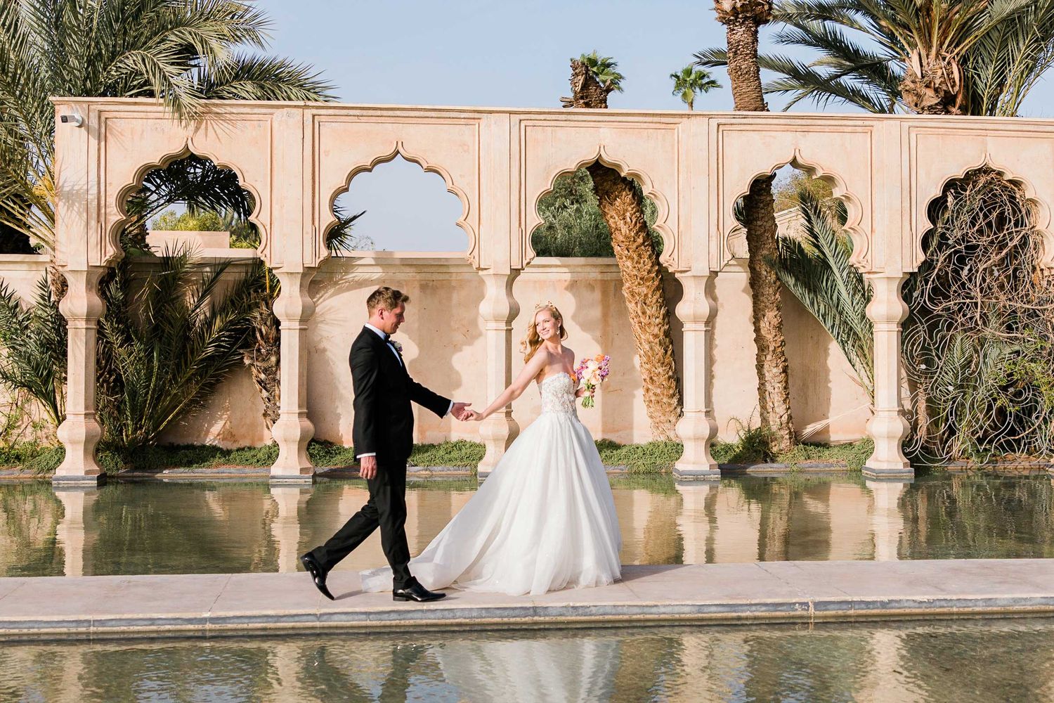 Wedding photo session at luxurious desert palace with palm trees and arched walkway at Palais Namaskar, Morrocco.
