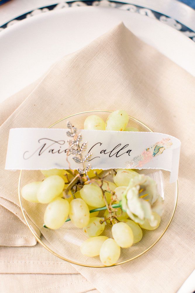 Elegant place card holder with fresh green grapes displayed on a white plate against a light neutral background.