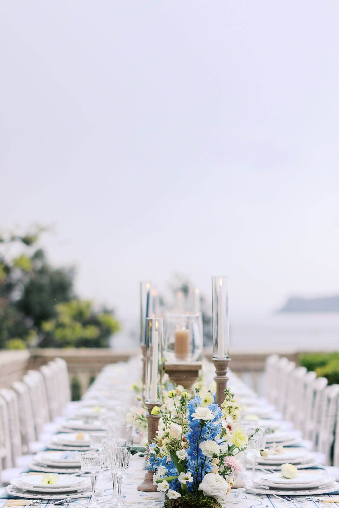 Elegant outdoor wedding reception table setting with blue and white flowers and crystal glassware overlooking the lake at Isola del Garda.