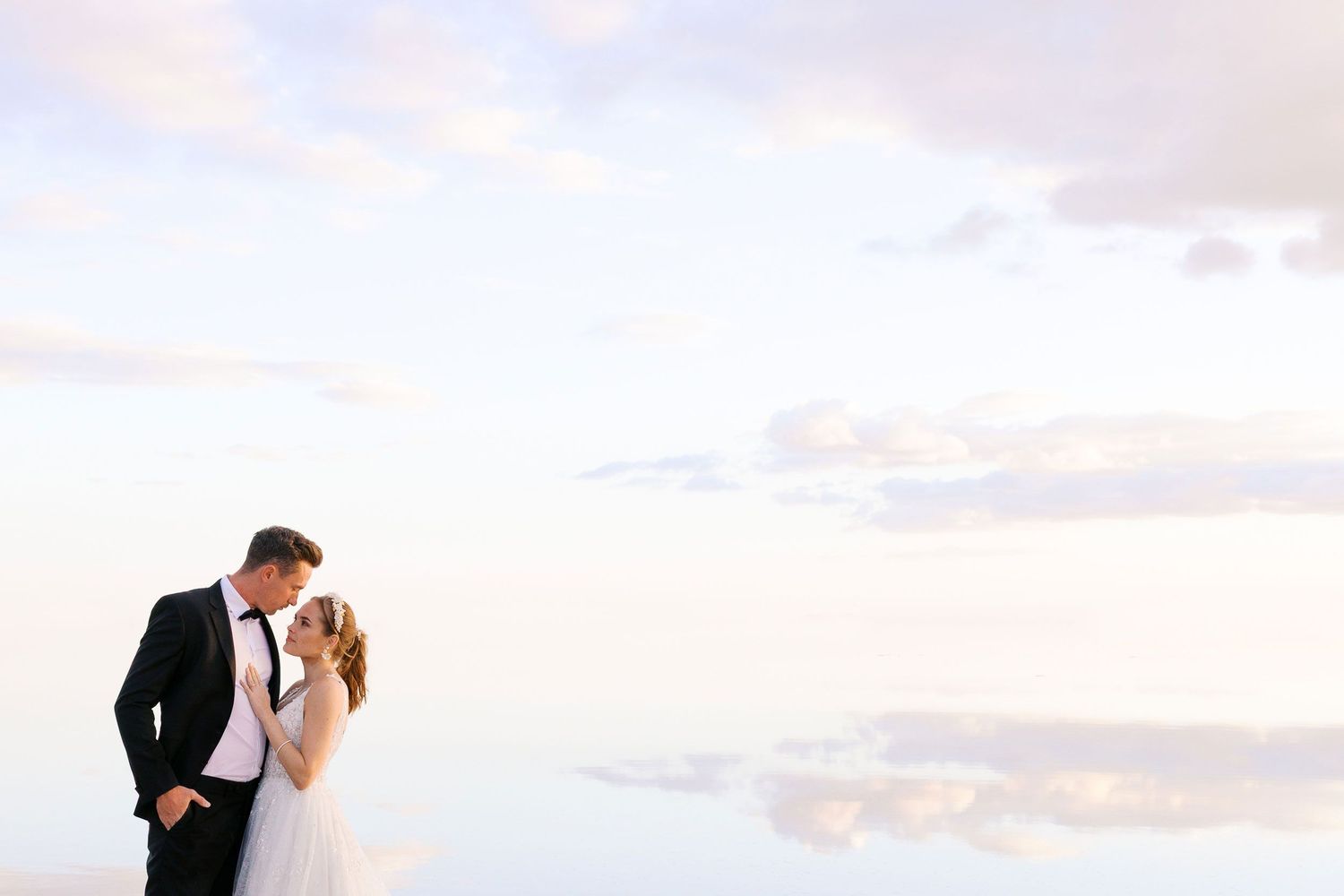 A bride and groom share an intimate moment against a dreamy cloudy sky backdrop.