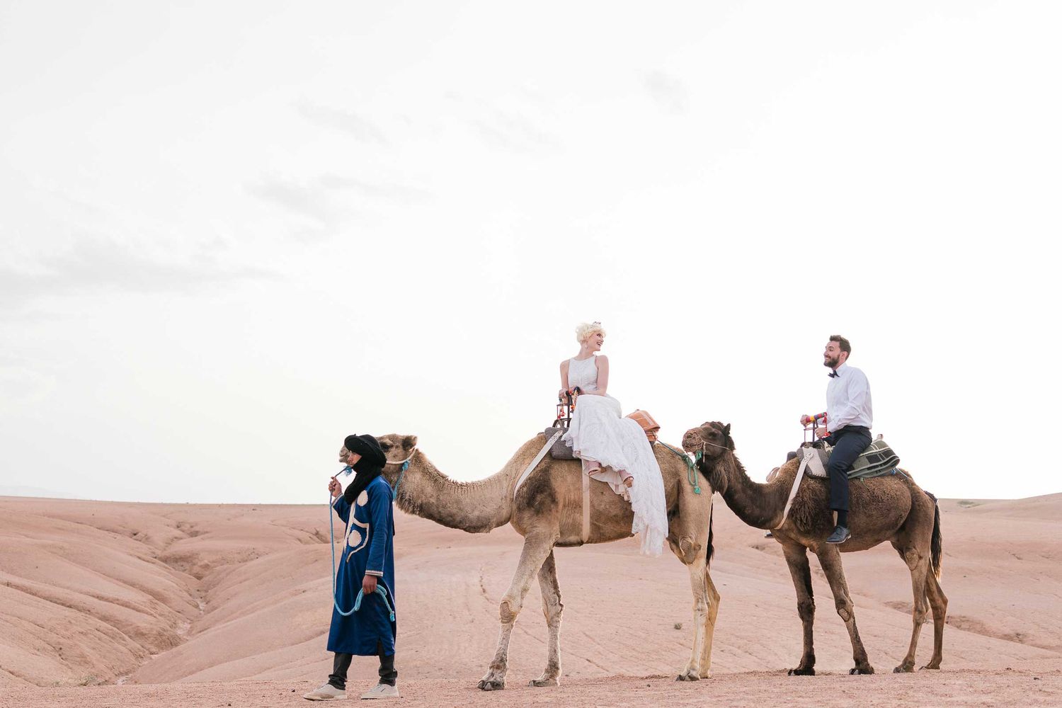 Desert wedding photoshoot with camels against sandy dunes backdrop.