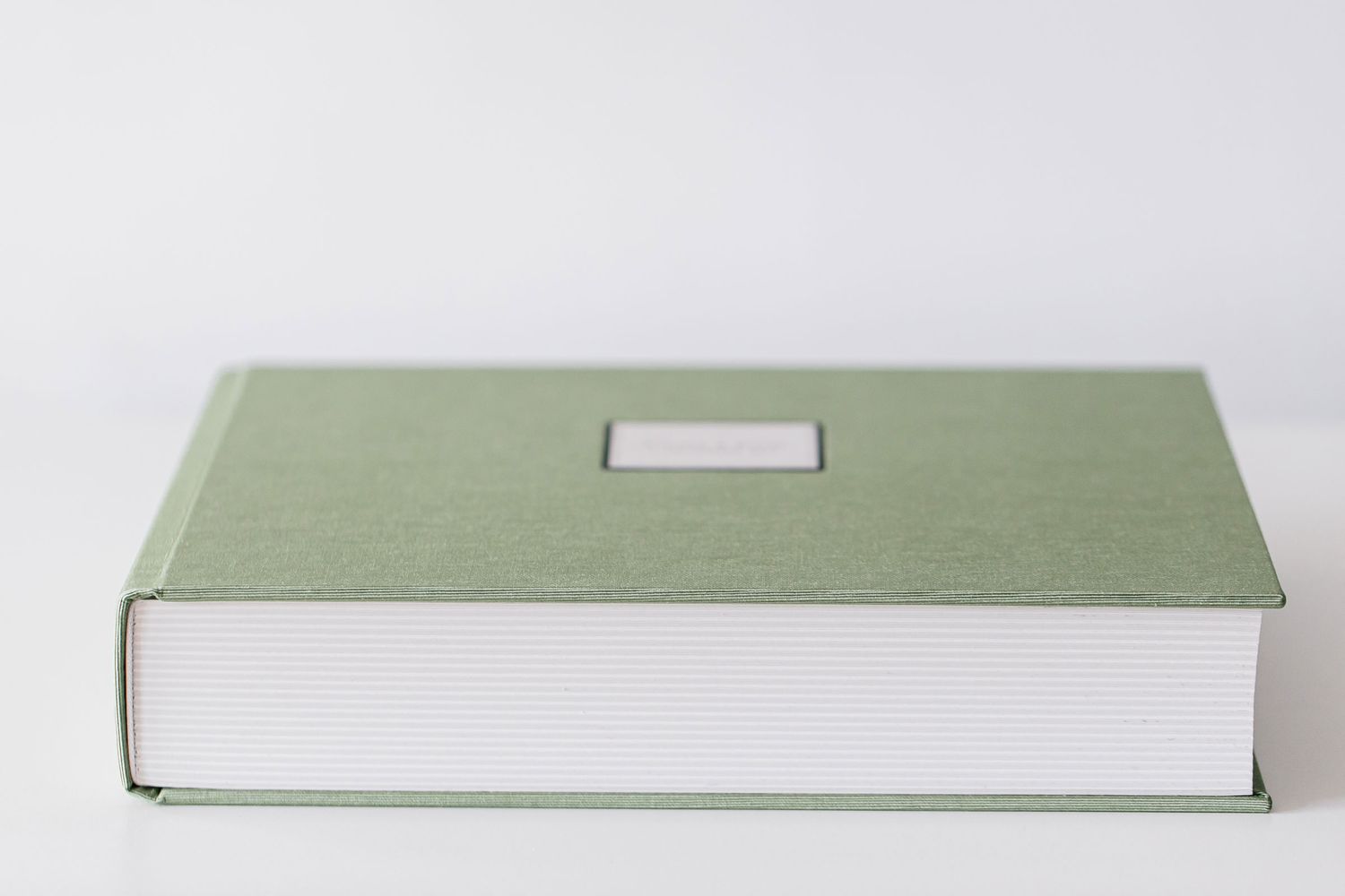 Minimalist white and sage green wedding album displayed on plain background.