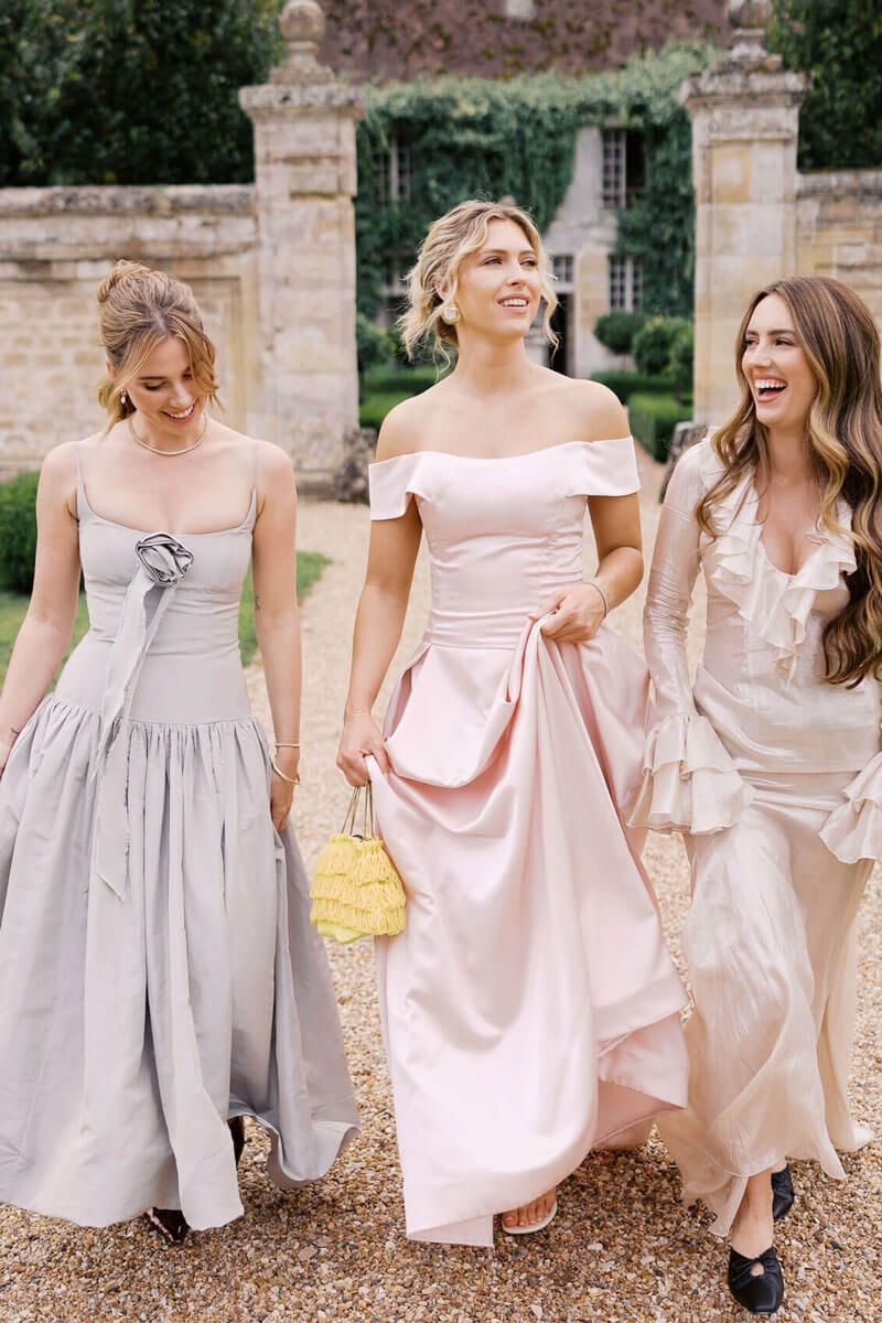 A group in pastel pink and gray dresses laughs and twirls together on a stone patio outside a historic building at Chateau de Villette.
