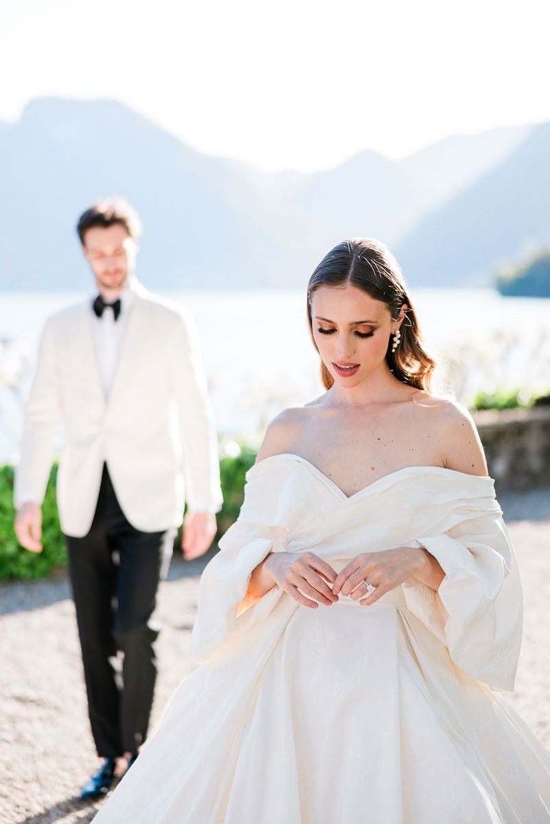 An elegant bride in a white off-shoulder gown poses at Lake Como Villa Balbiano