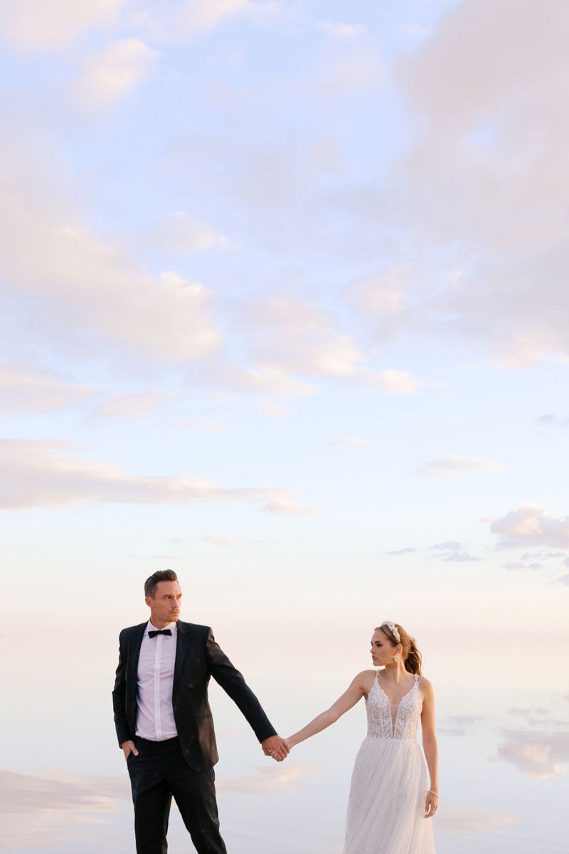 A romantic beach wedding photoshoot with a couple walking together against a sunset sky.