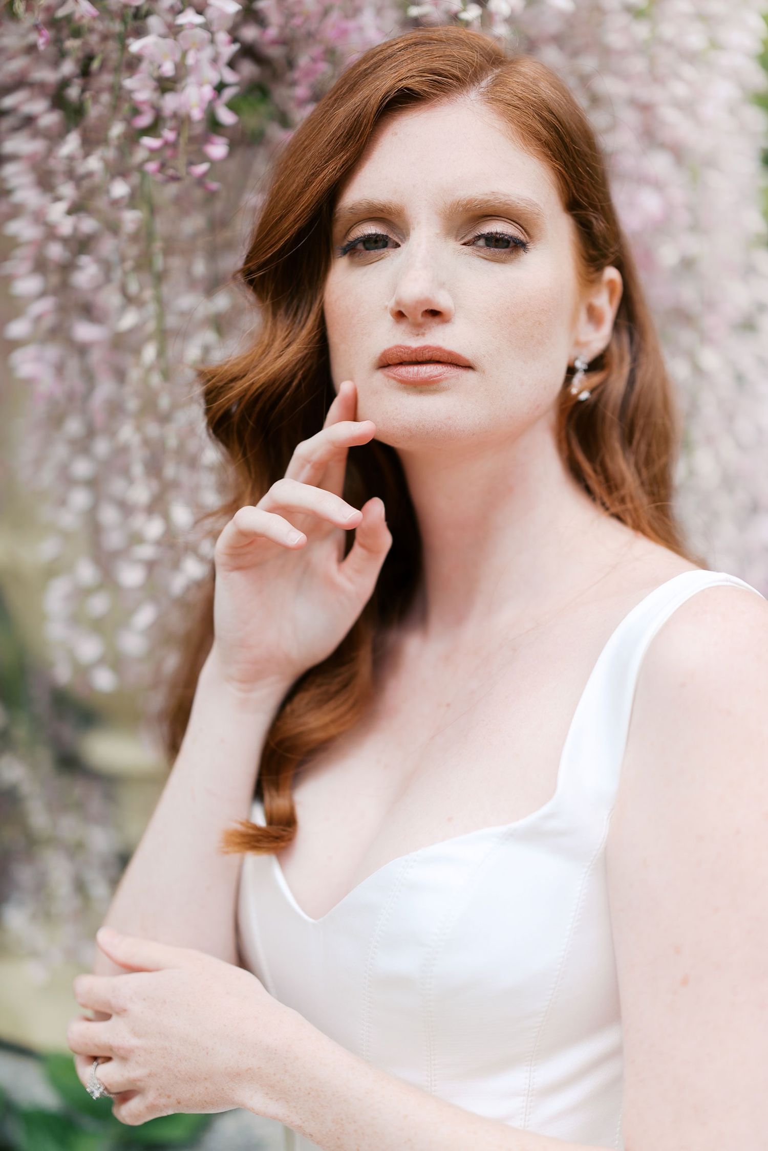 Ethereal spring bridal portrait with delicate cherry blossoms framing a figure in a white dress against a soft pink background.