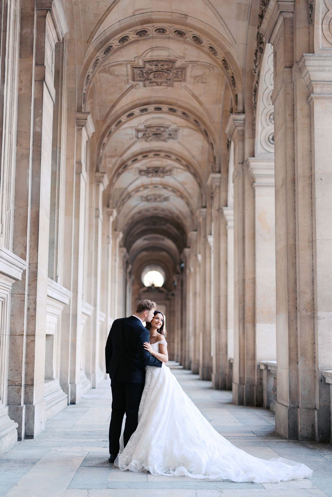 Wedding couple photographed in elegant arched corridor with repeating stone columns.