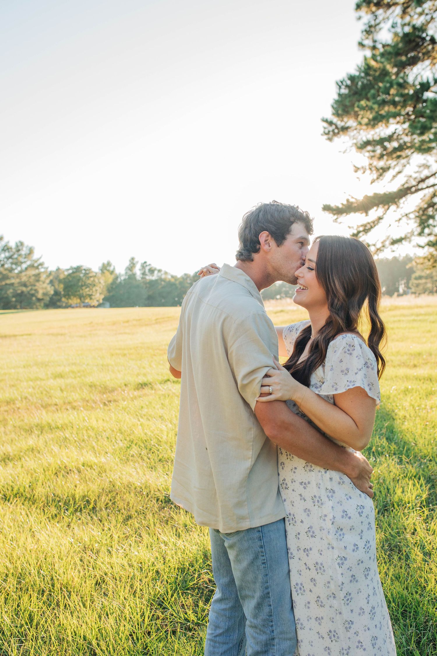 Romantic couple embraces in a sunlit meadow during golden hour, creating a dreamy summer scene.