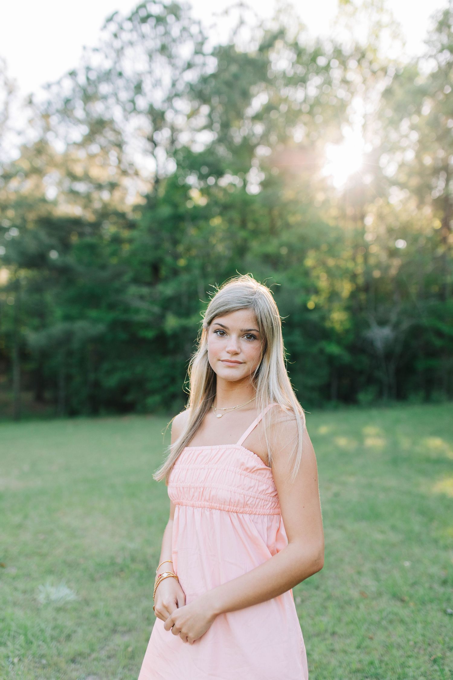 Woman in flowing pink dress standing in sunlit field during portrait session.