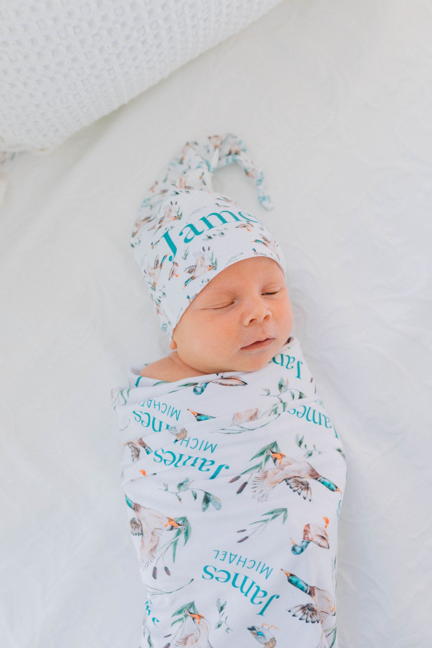 Sleeping newborn wearing white and blue patterned outfit with matching hat on white background.