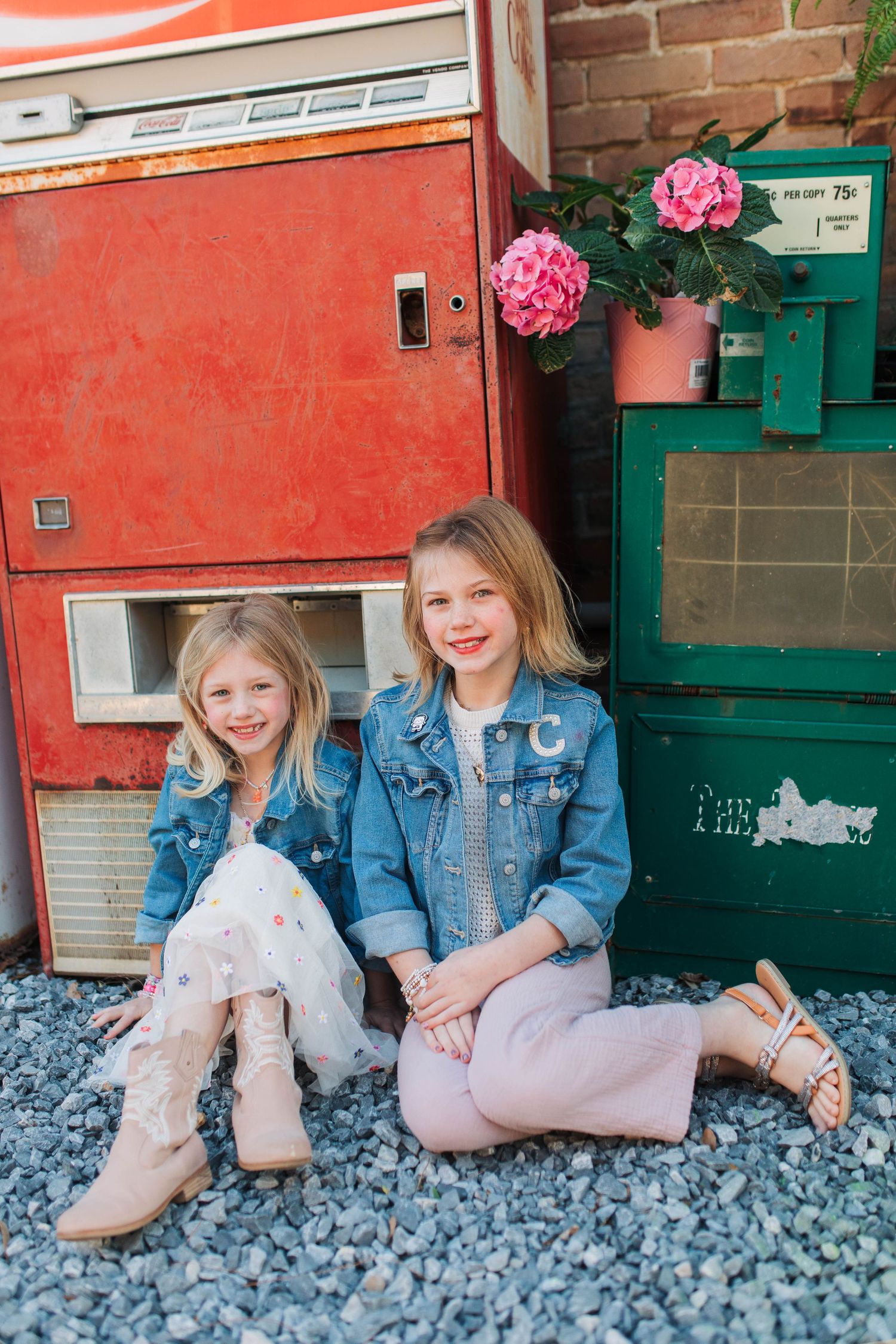 Children's feet in pink boots lined up against a coral wall with blue stones and green accents.