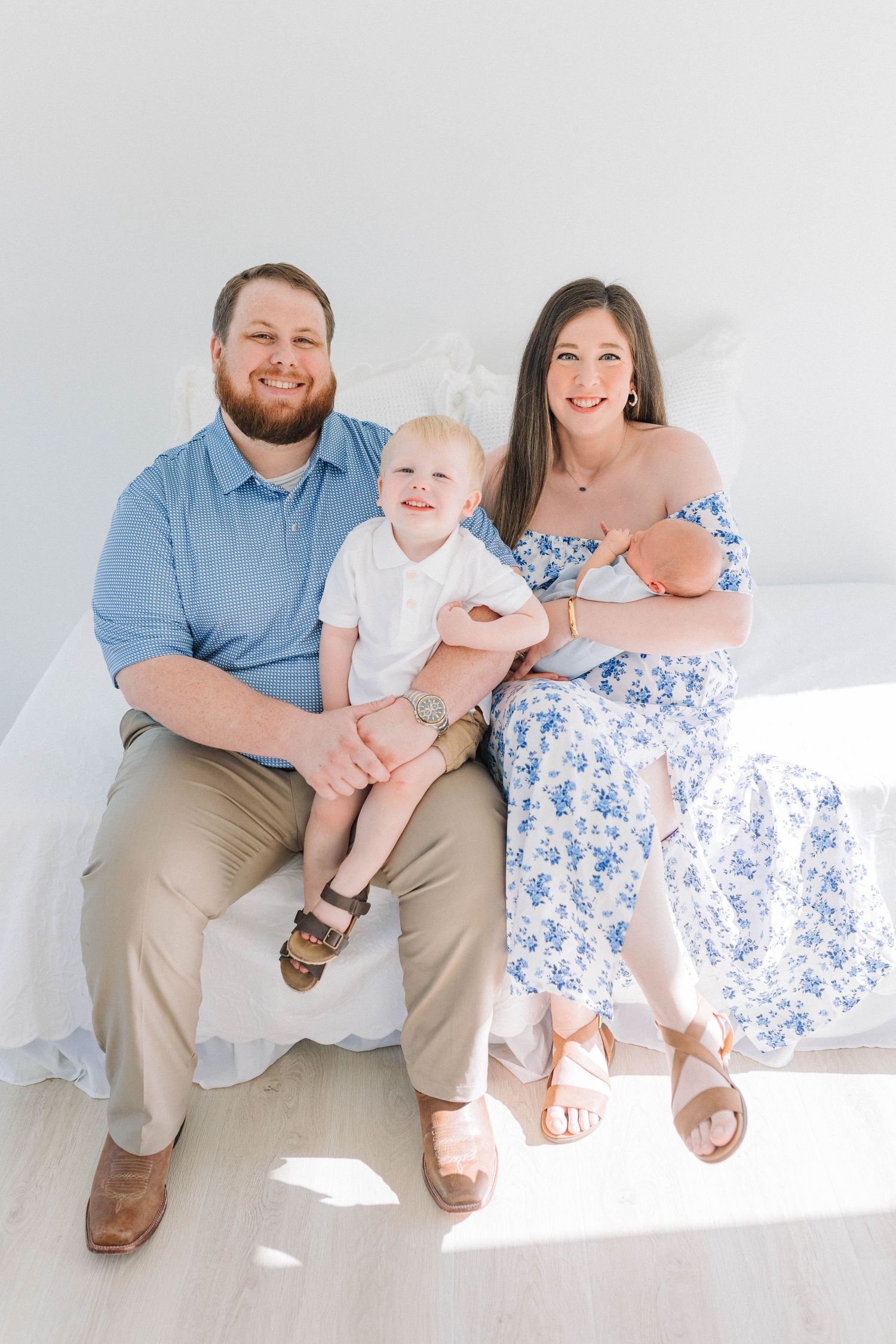 Family sits together on white backdrop wearing coordinating blue and white outfits.