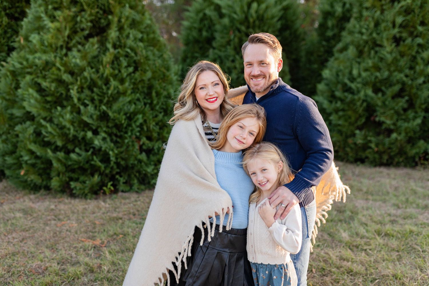 Family portrait session with cream blanket against evergreen trees.