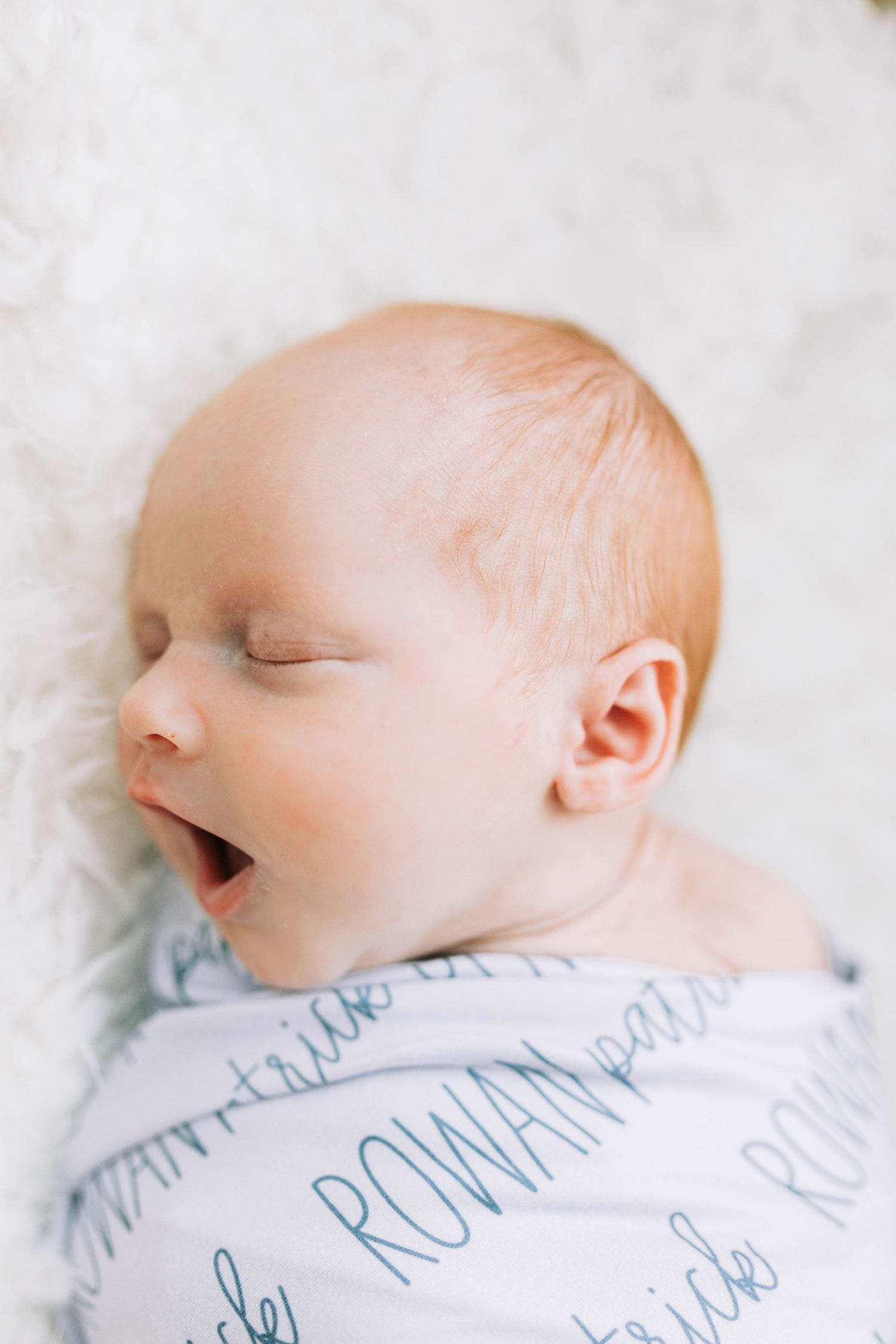 Sleeping newborn wrapped in text-patterned swaddle blanket.