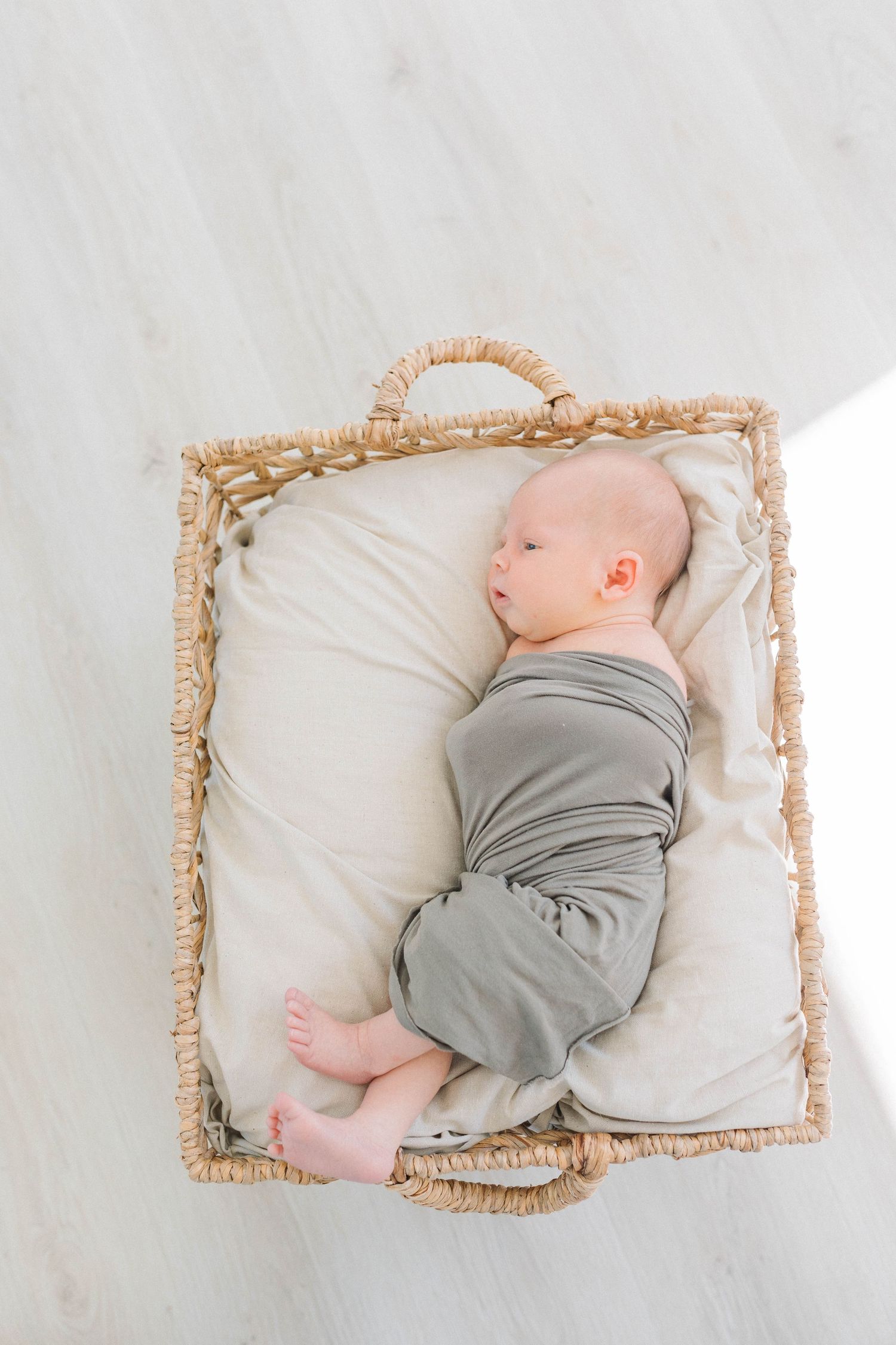Sleeping baby in grey outfit lying in woven basket with white cushioning.
