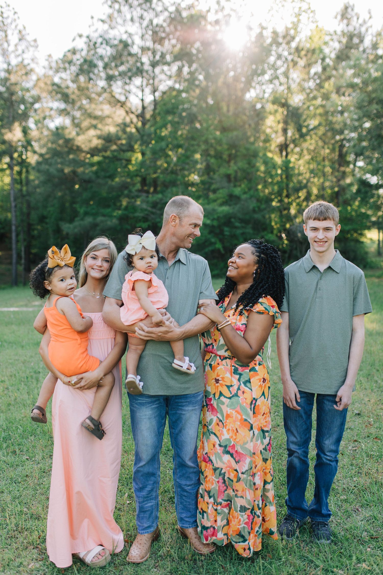 Family group poses playfully together outdoors in coordinated casual outfits.