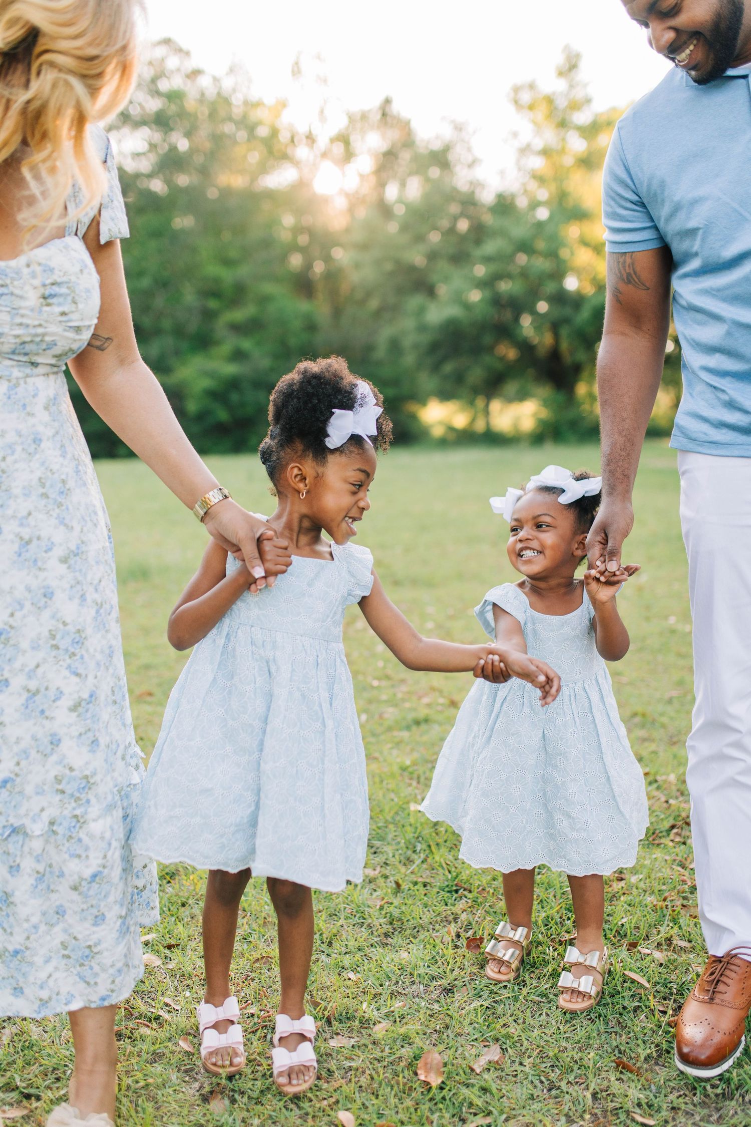 Family members wearing coordinating blue and white outfits hold hands while walking in a grassy field.