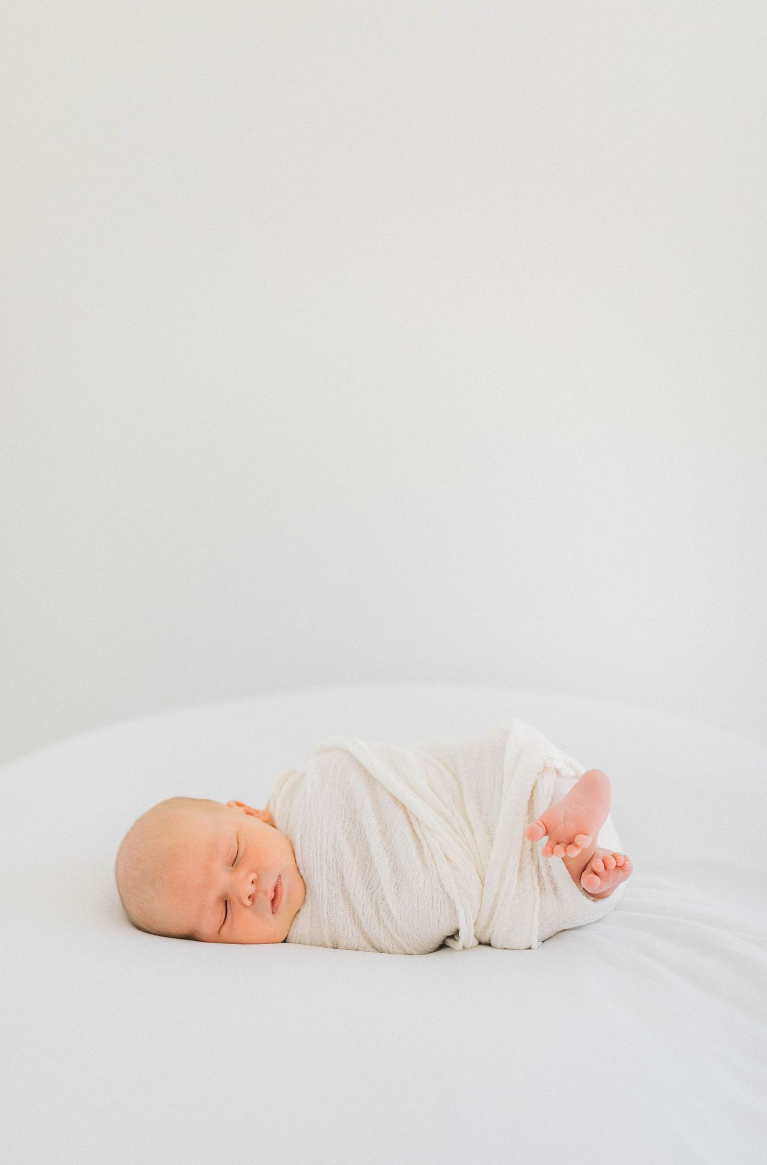 Peaceful sleeping newborn wrapped in white fabric against clean white background.