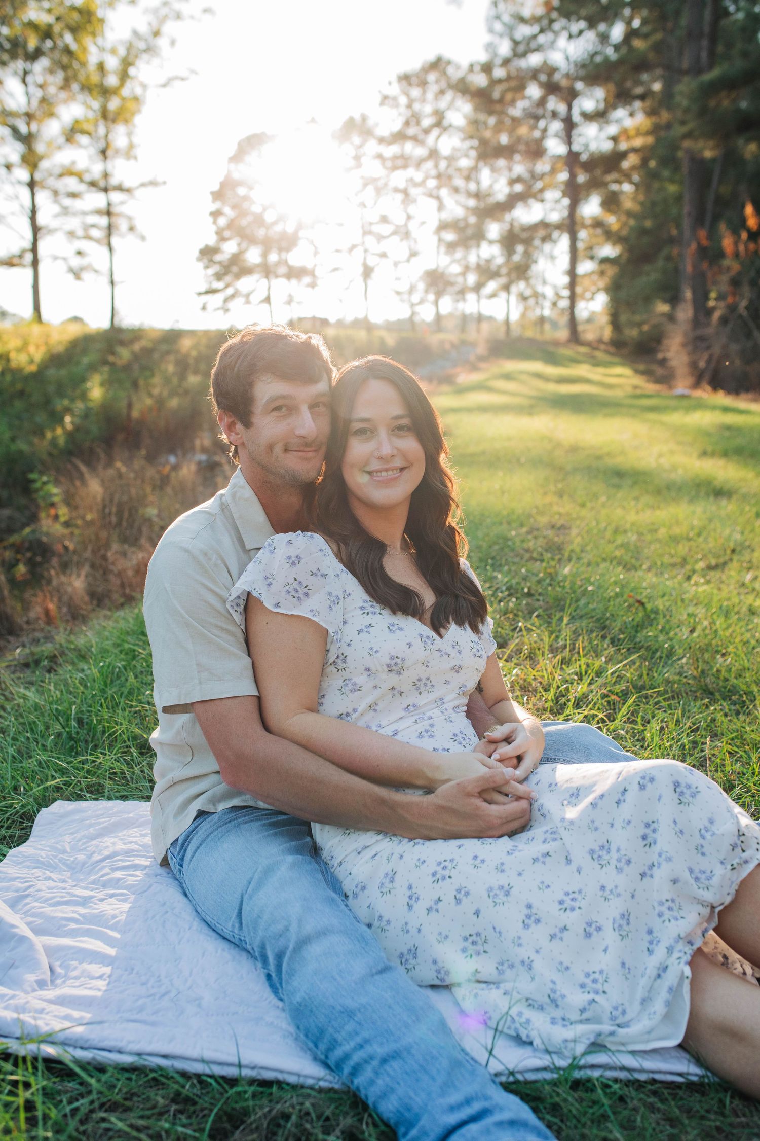 Couple lounging on white blanket in sunny meadow.