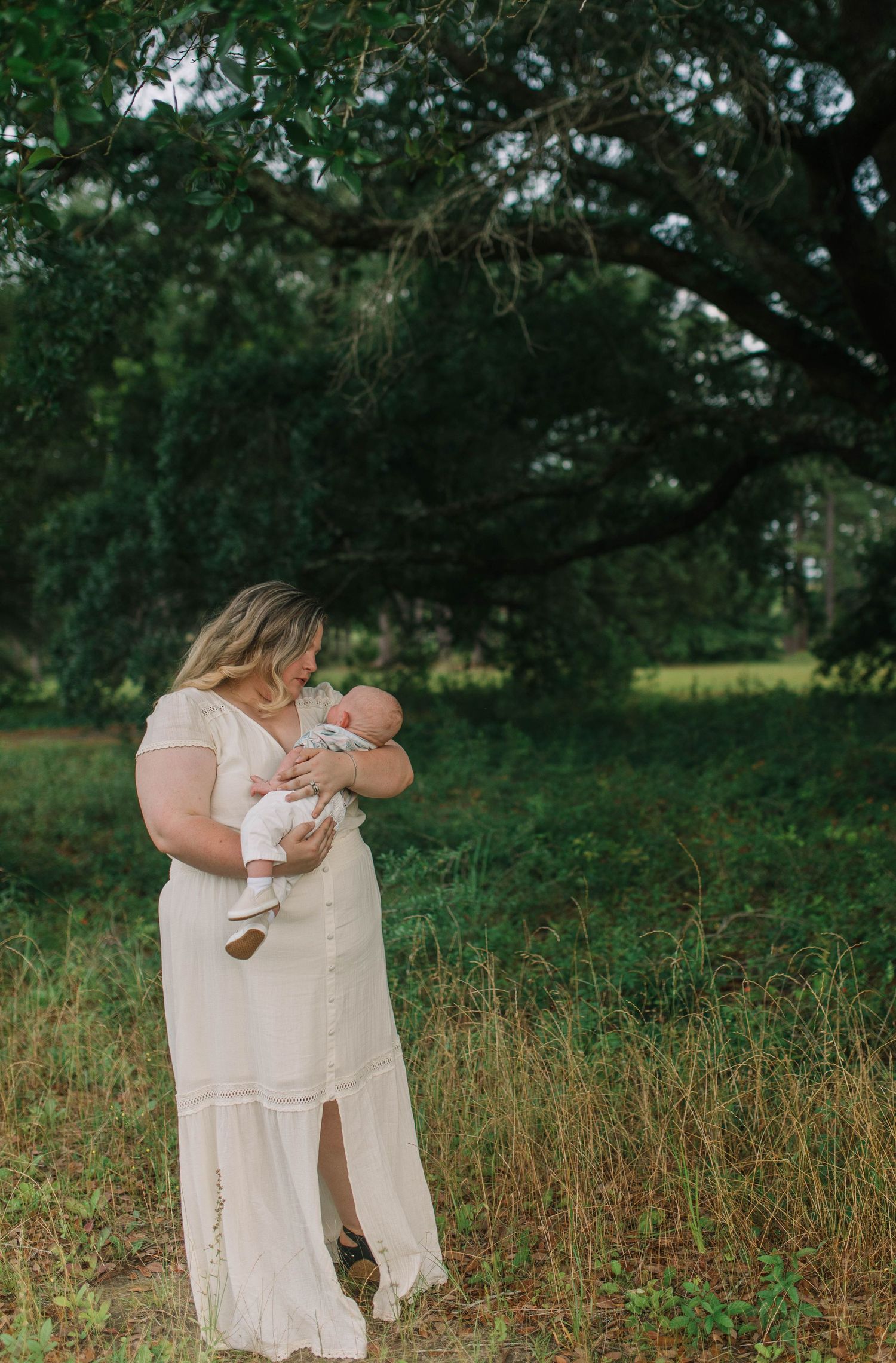 Tender moments captured in a field with soft natural lighting and cream-colored clothing.