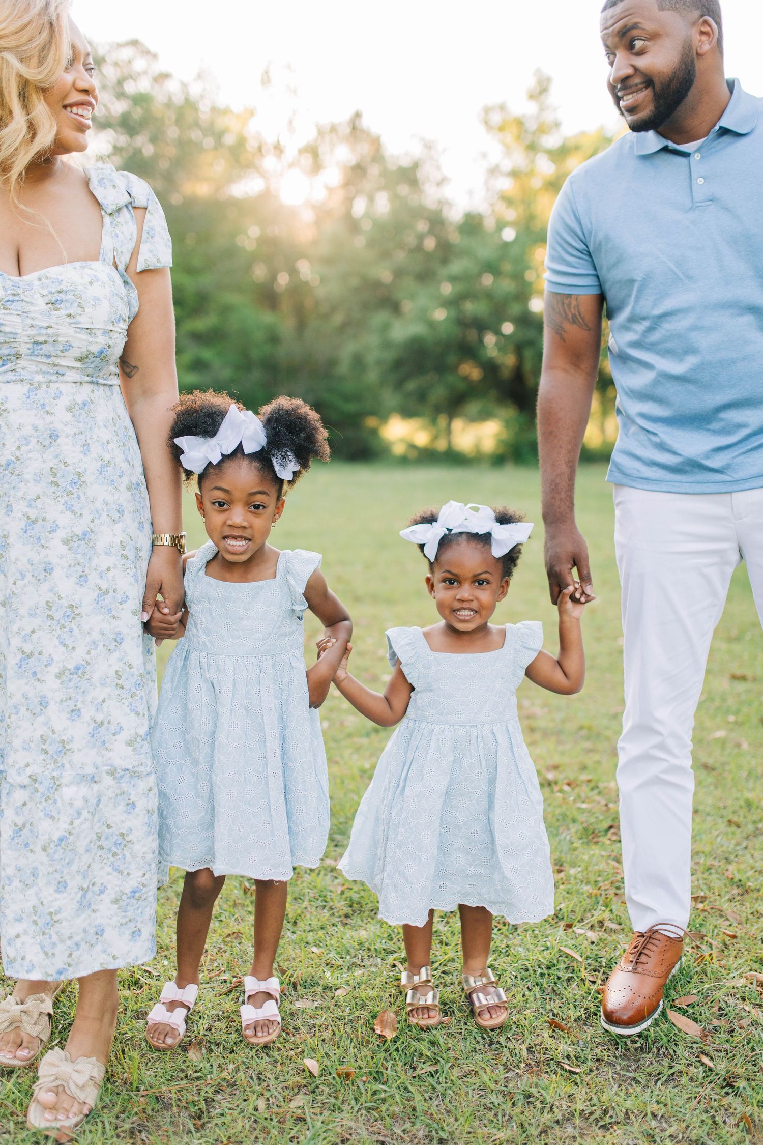 Family wearing coordinated blue and white outfits holds hands in grassy field.