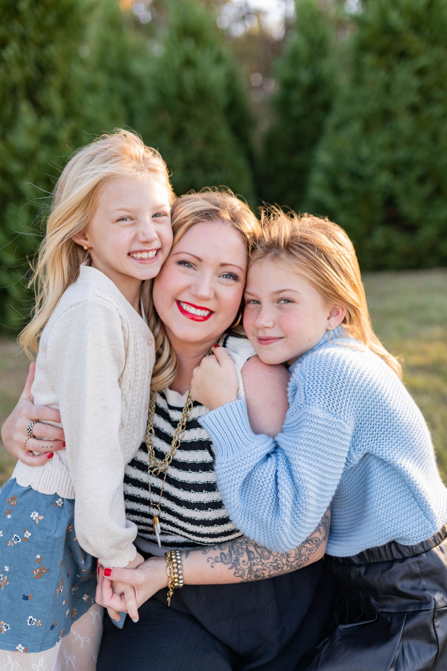 Three people share warm hugs and laughter during an outdoor family photoshoot.