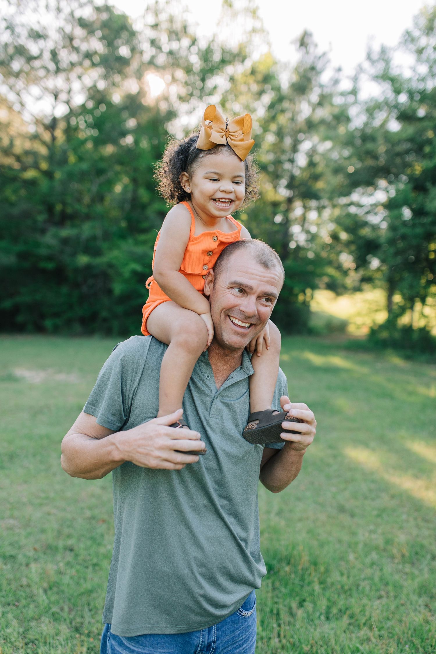 Playful moment between parent and child in orange shirt on grassy field.