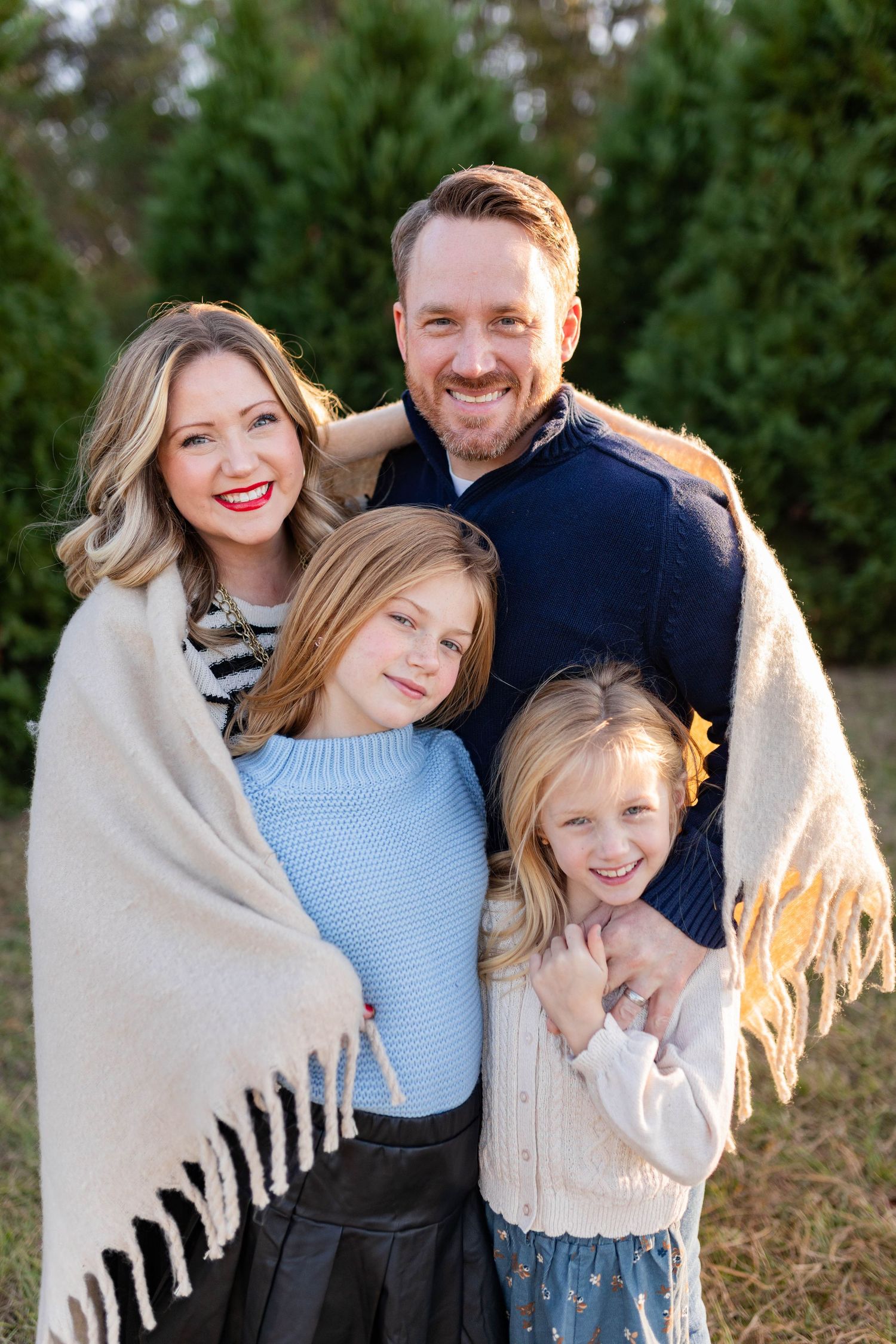 Family of four wrapped in cream blanket share intimate moments outdoors.