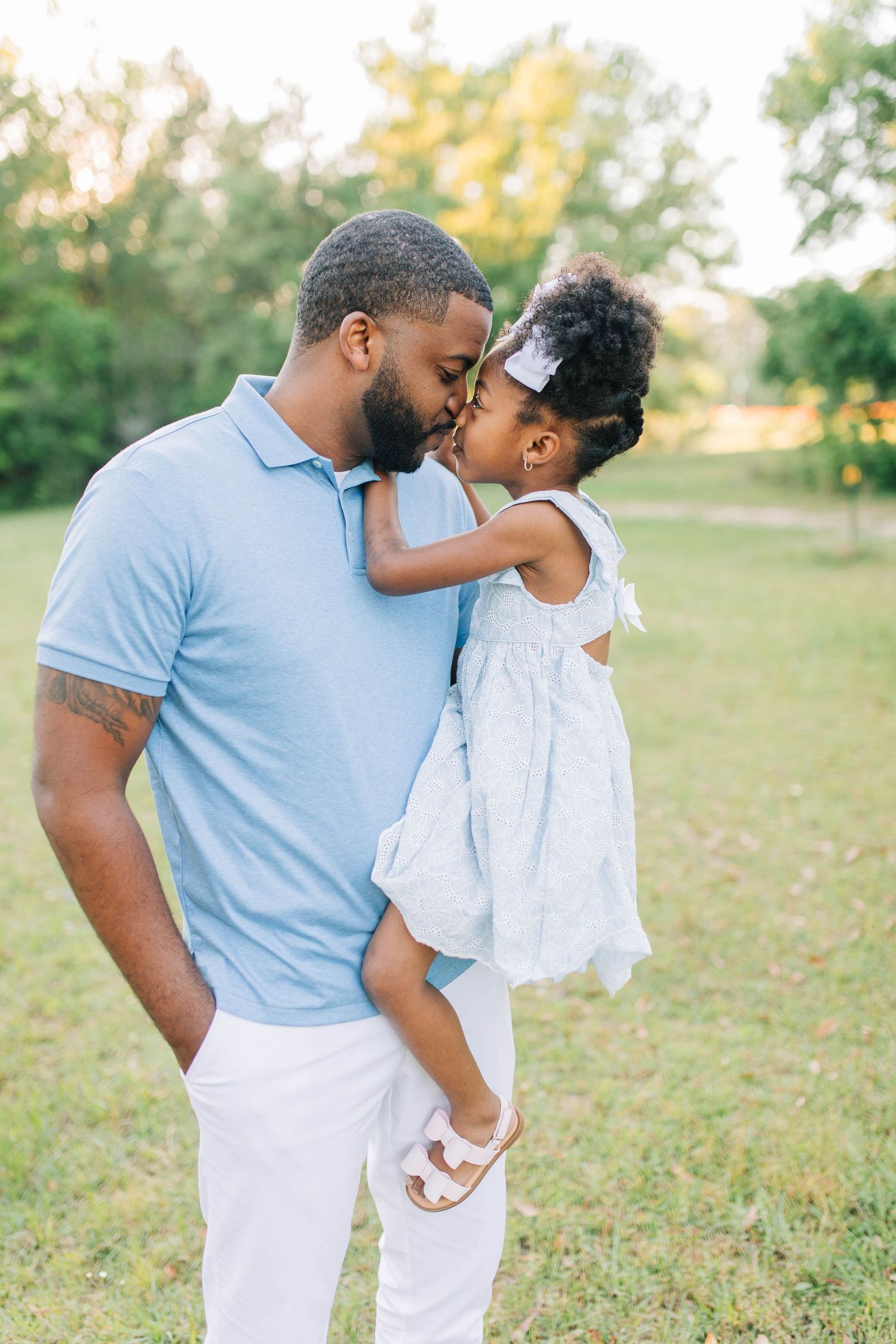 Tender father-daughter moments captured in a grassy field during sunset.