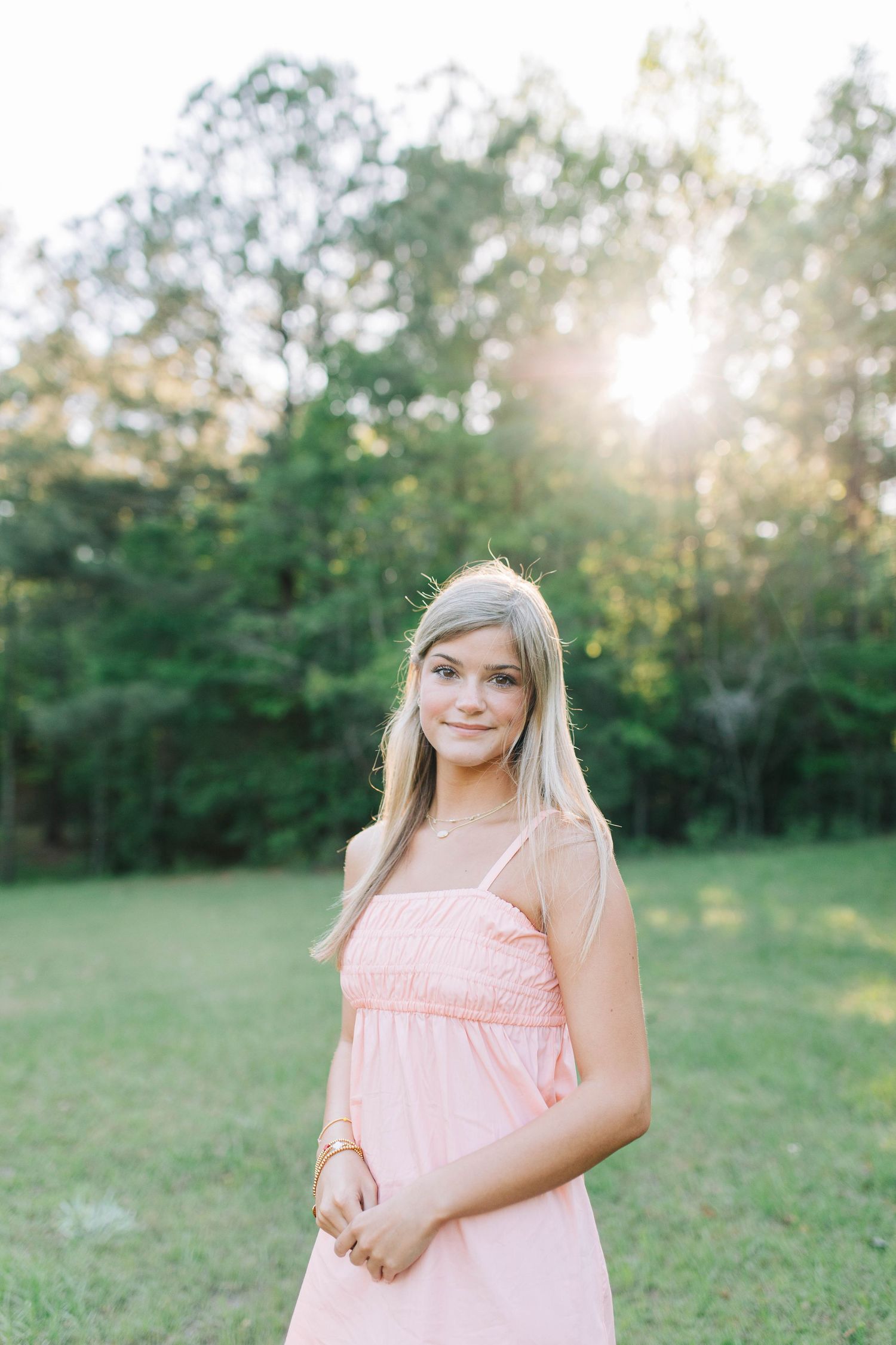 Young person in pink dress poses in grassy field during sunset photoshoot.