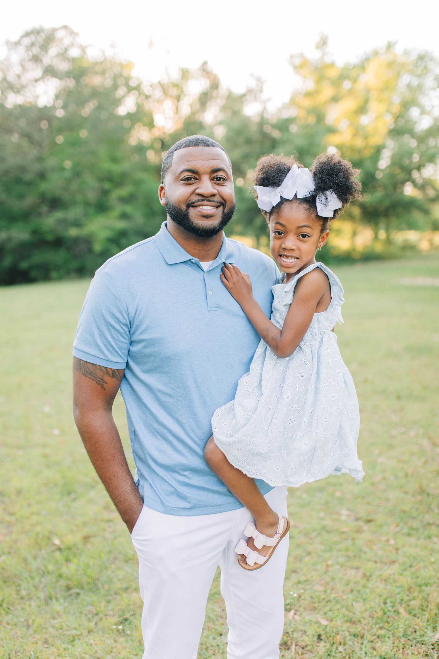 Father and daughter share playful moments in coordinated blue and white outfits outdoors.
