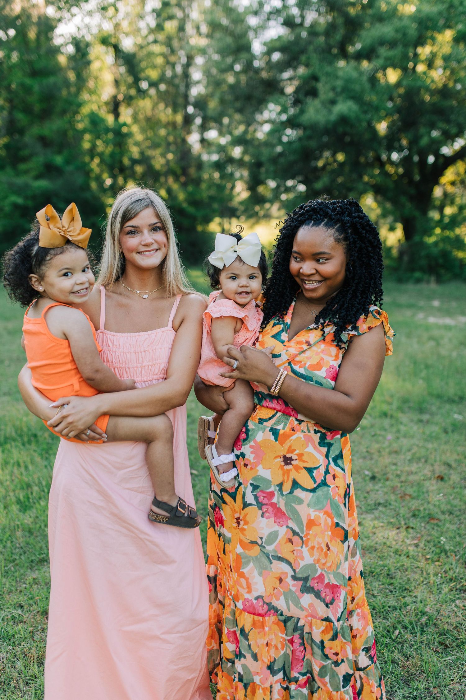 Friends in coral and floral dresses share laughs during golden hour photoshoot.