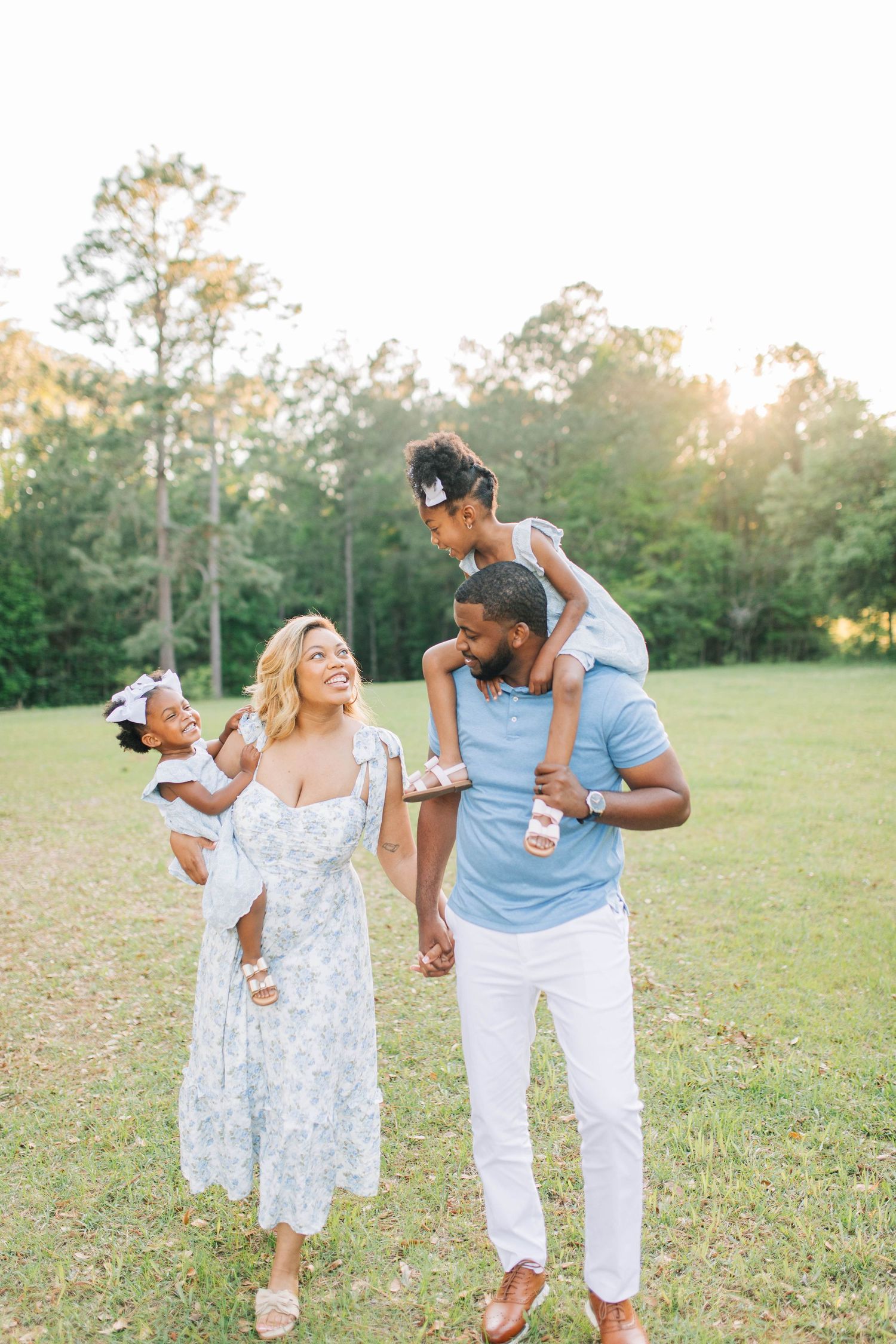 Family playing and dancing together in grassy field during sunset photo session.
