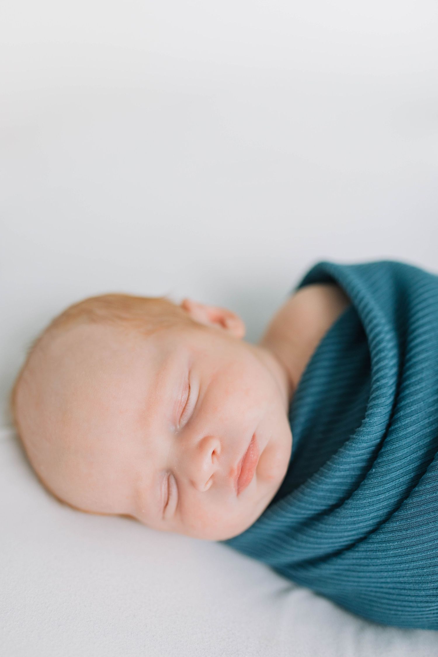 Close-up of sleeping baby with teal wrap against white background.