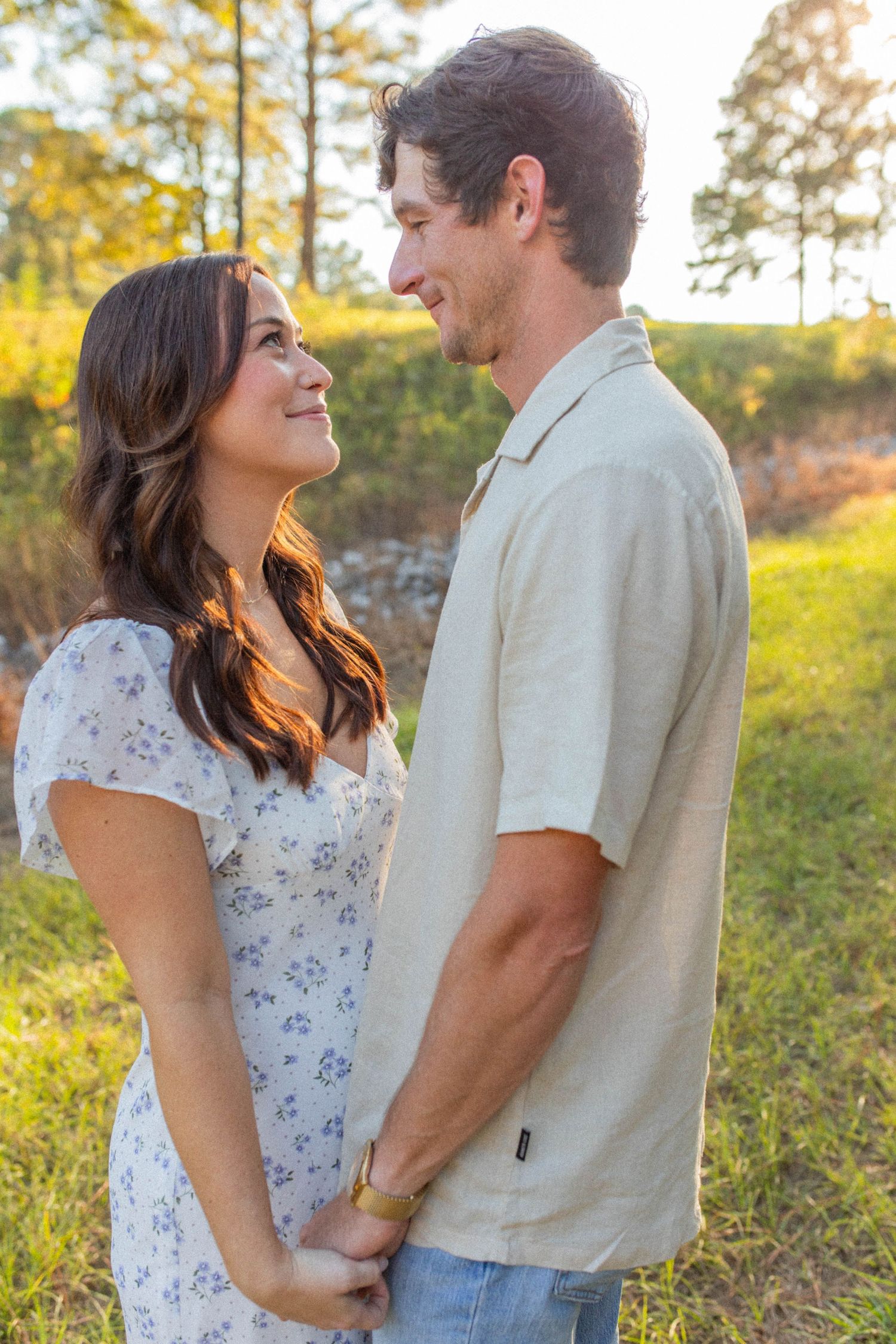 Couple sharing tender moment on sunny hillside in casual summer attire.