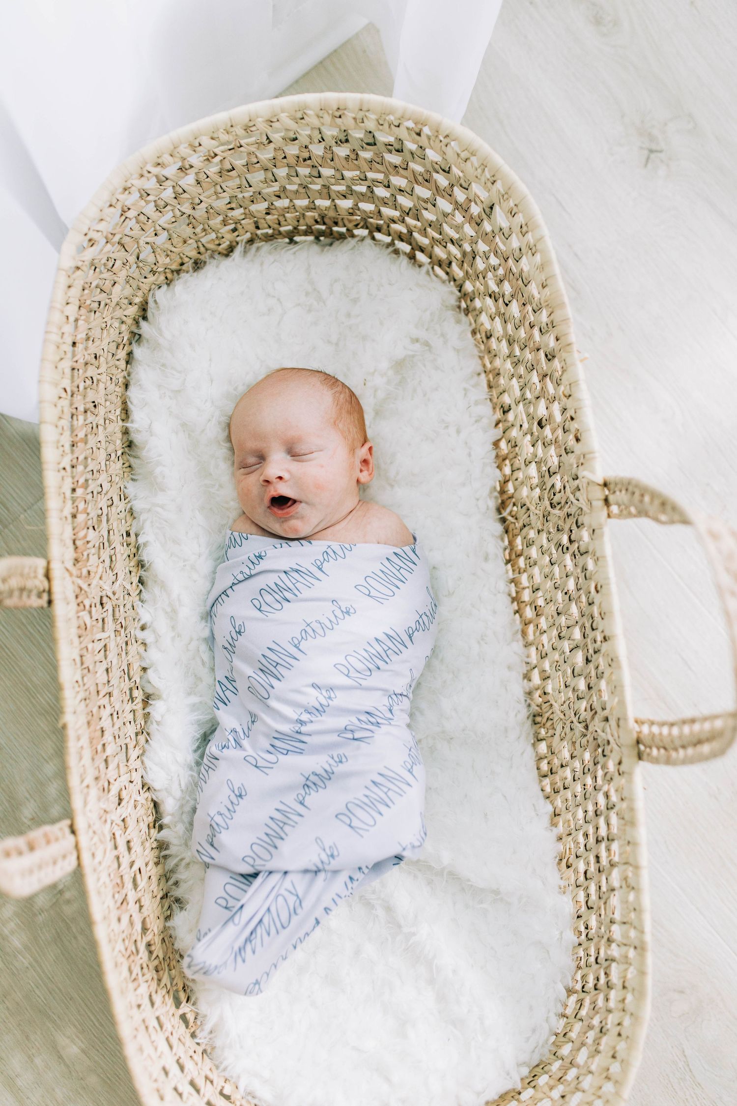 Sleeping newborn in patterned swaddle blanket resting in woven moses basket.
